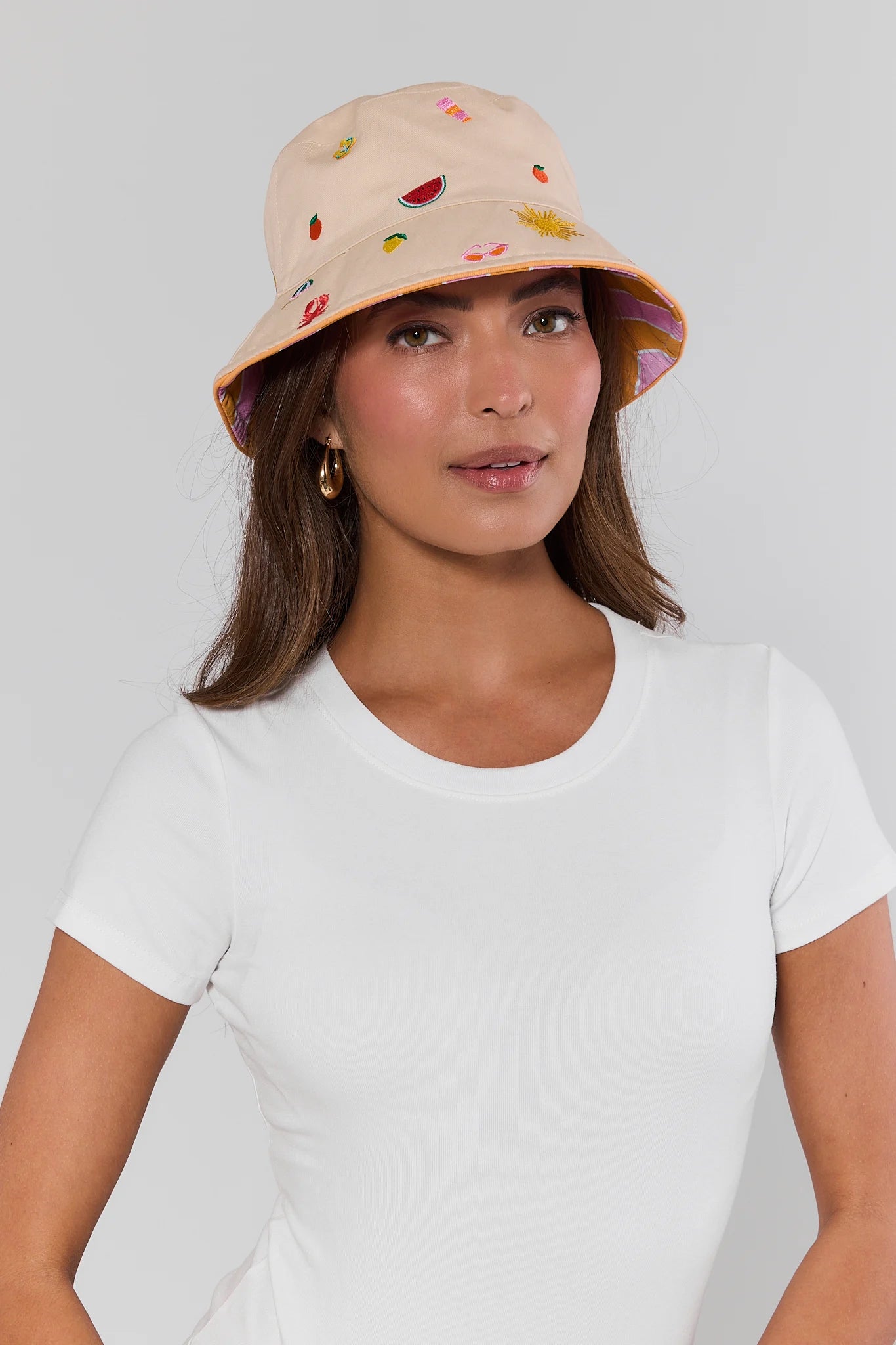 Woman wearing a beige bucket hat with colorful designs on a plain background