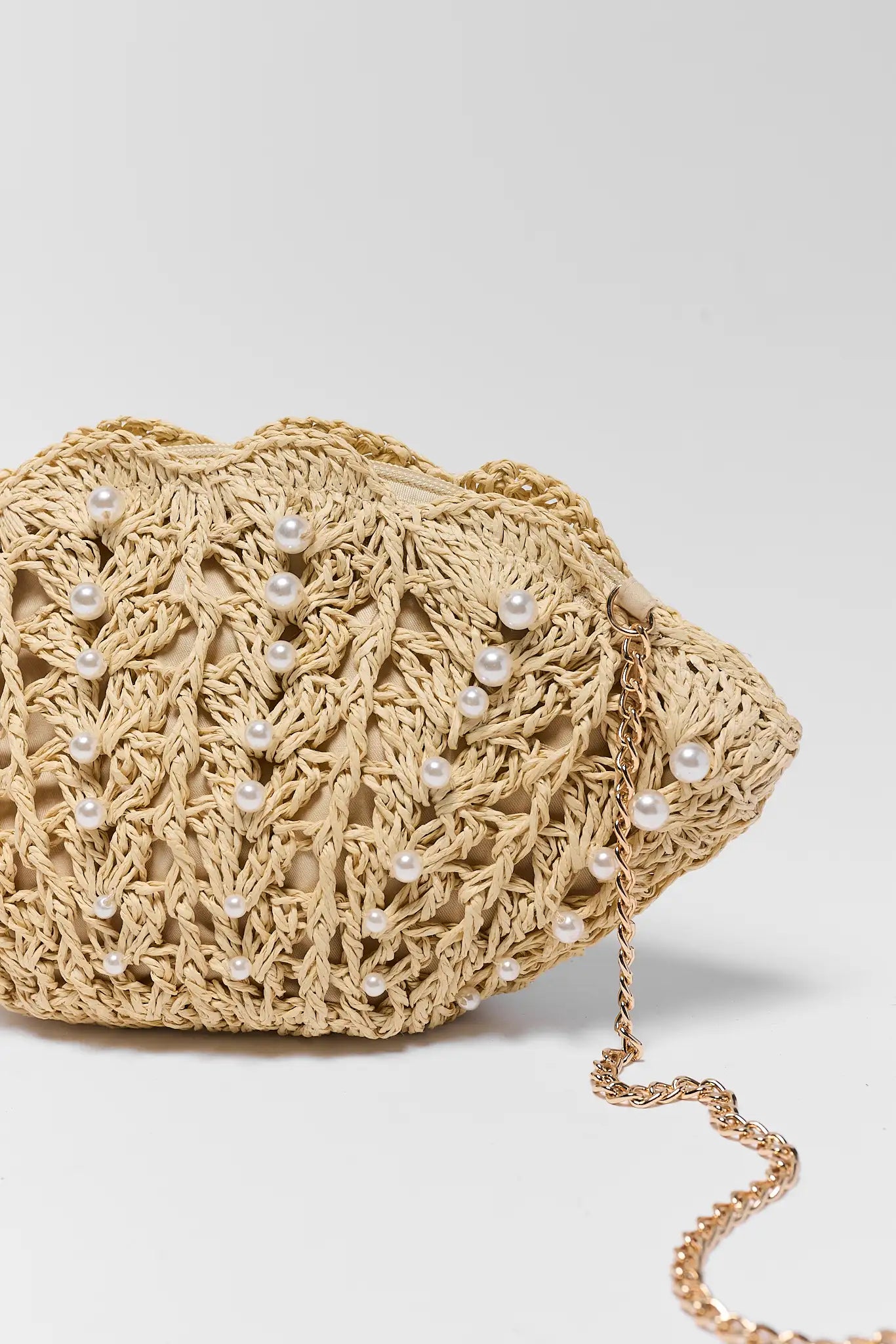 close up Beige crochet handbag with pearl embellishments on a light gray background