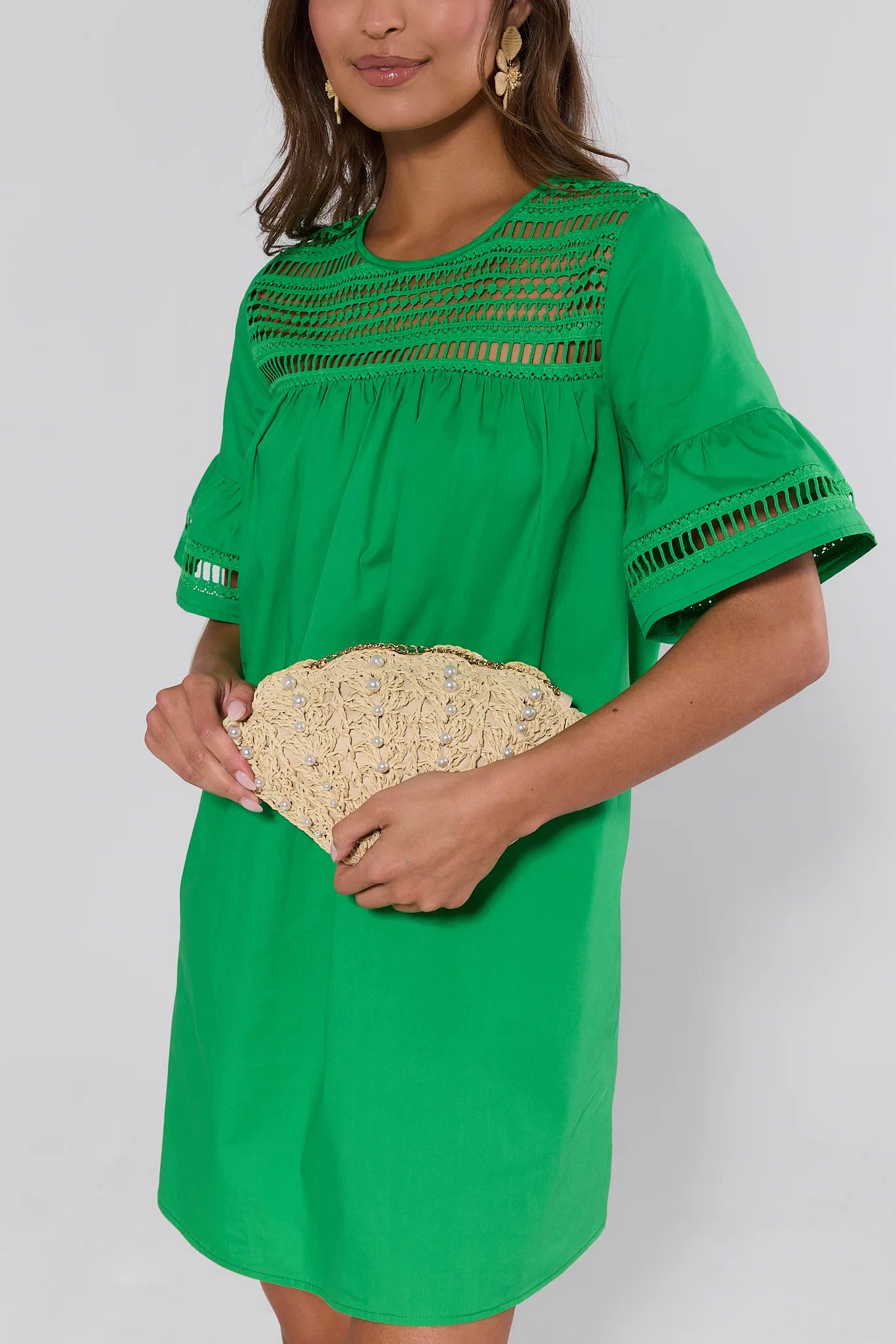 Woman wearing a green dress holding a woven clutch against a white background