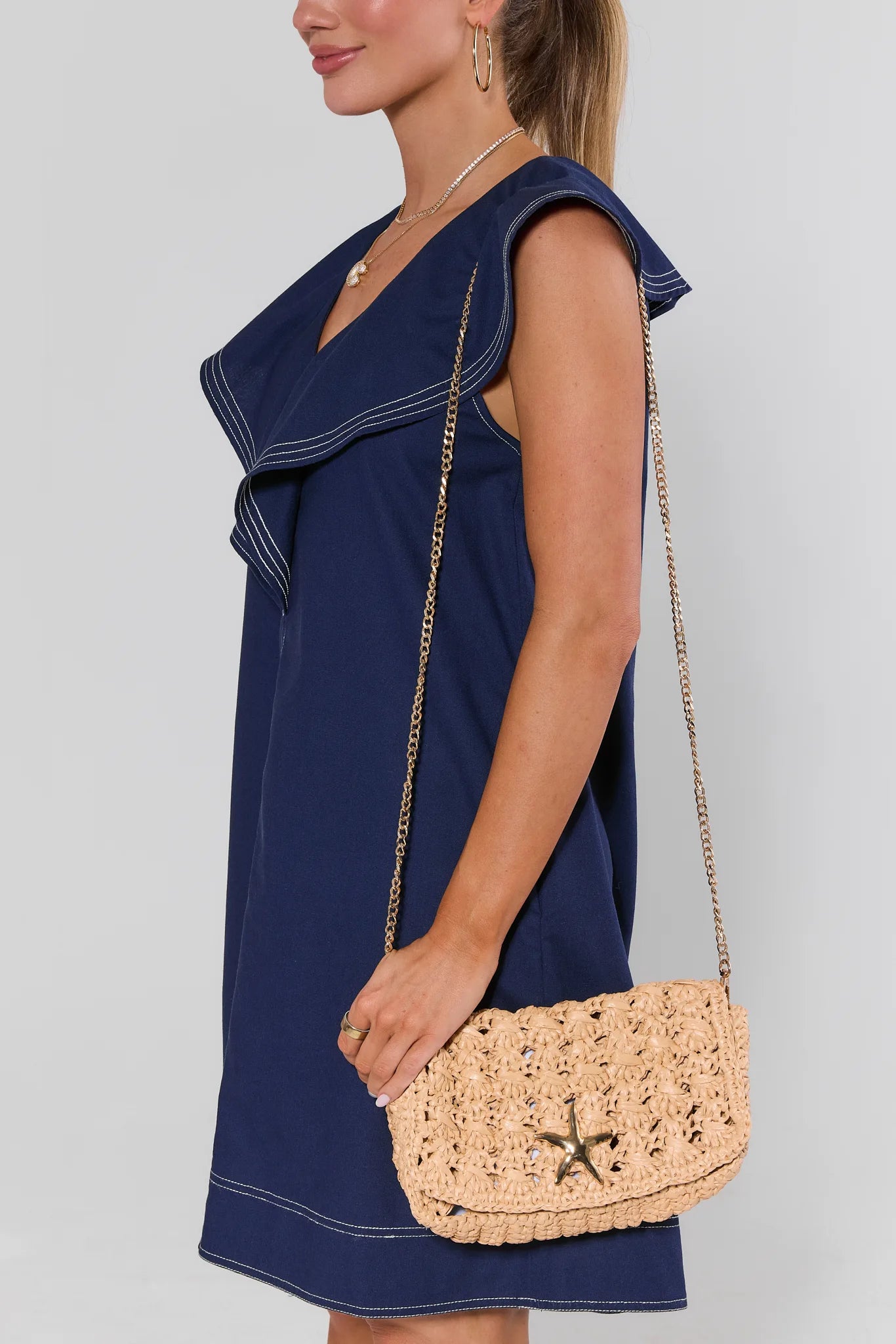Woman in a navy dress holding a woven beige handbag against a light gray background