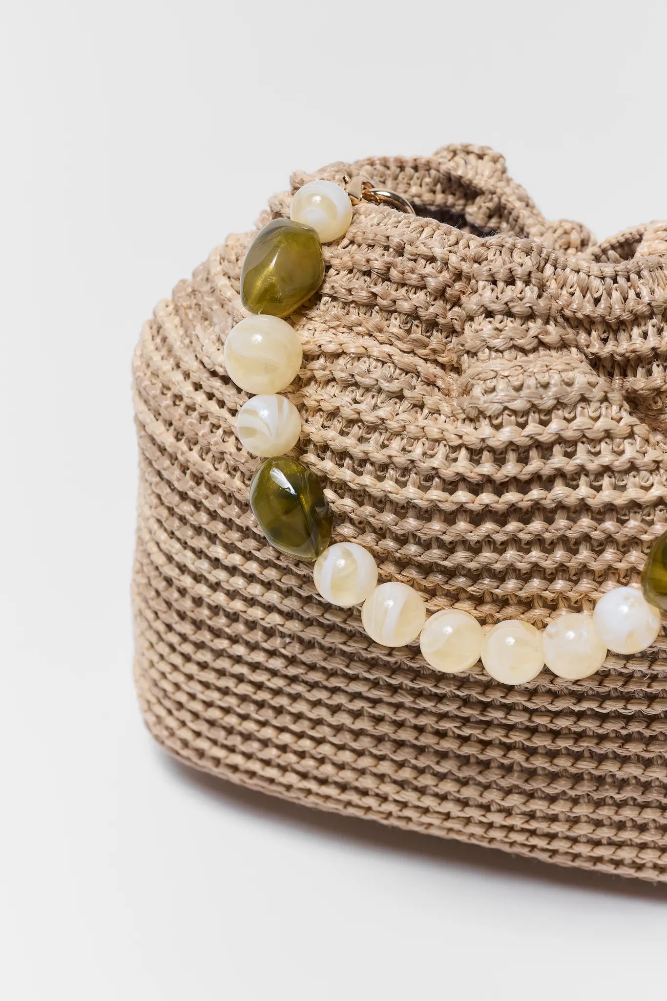 close up Beaded handle with green and white beads on a textured beige bag