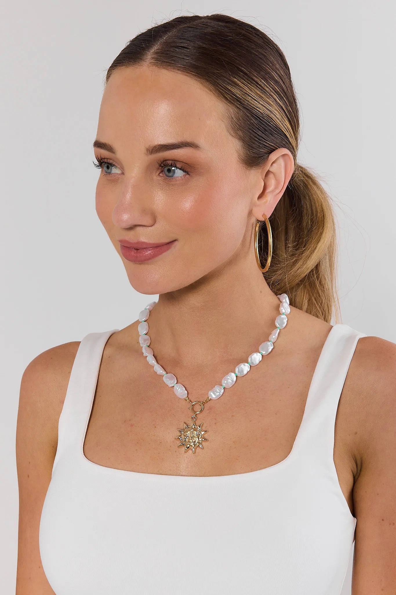 Woman wearing a pearl necklace with a gold pendant on a plain background