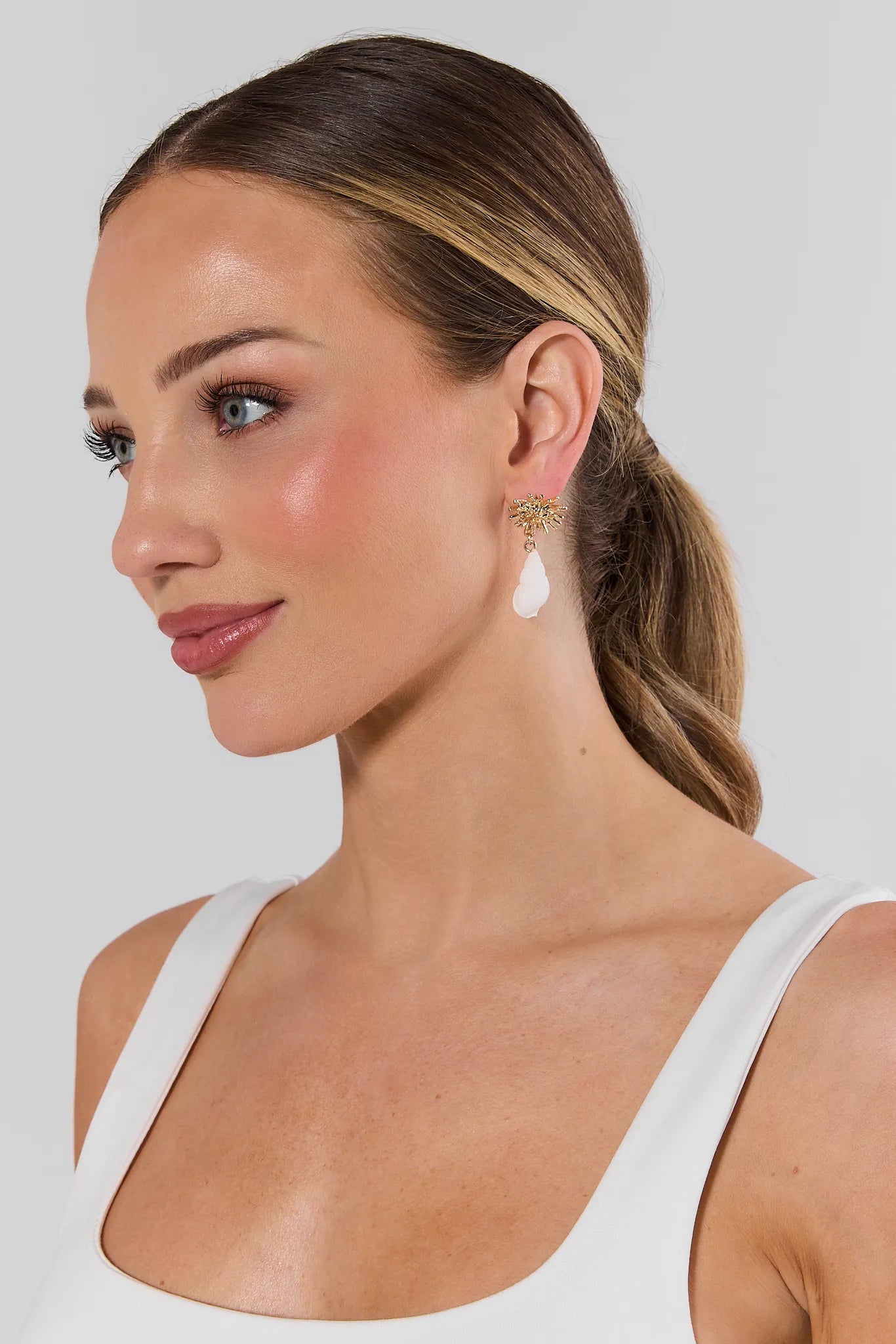 Woman wearing shell drop earrings with a plain background