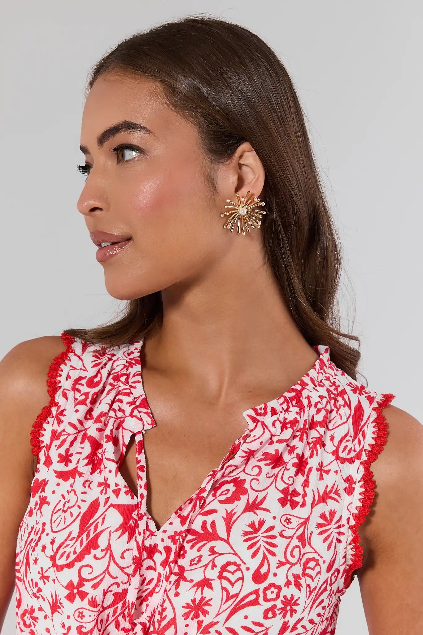 Woman wearing a red and white floral dress with gold earrings against a light gray background