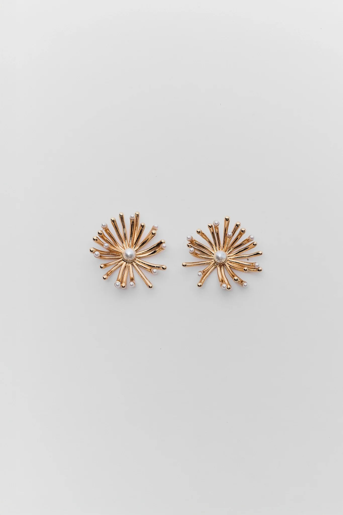 Pair of gold starburst earrings on a light gray background
