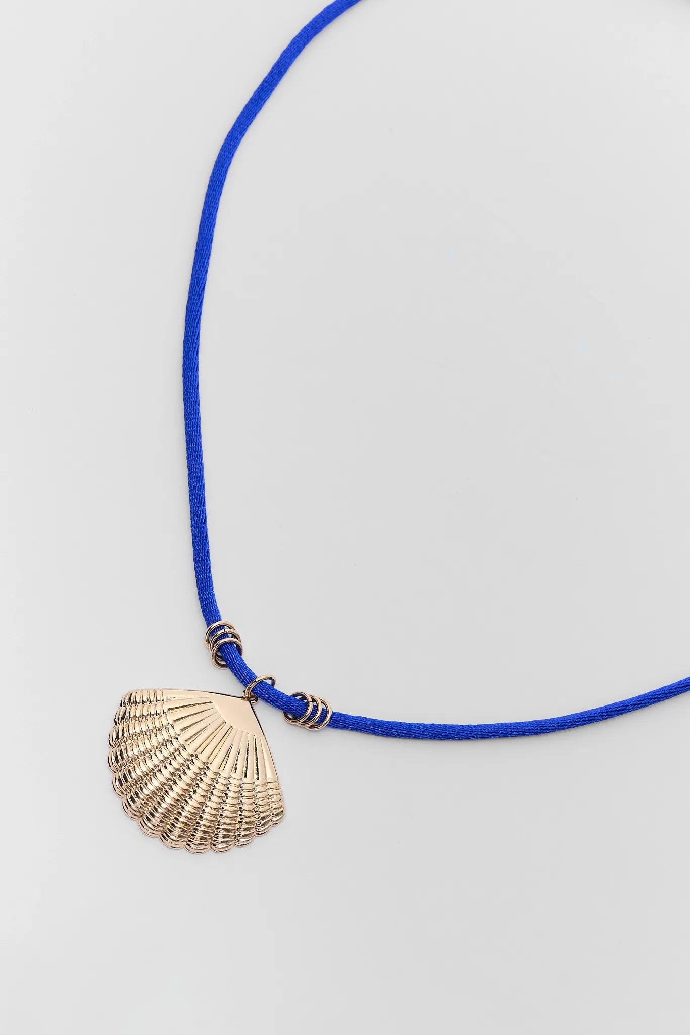 close up Necklace with a shell pendant on a blue cord against a light gray background