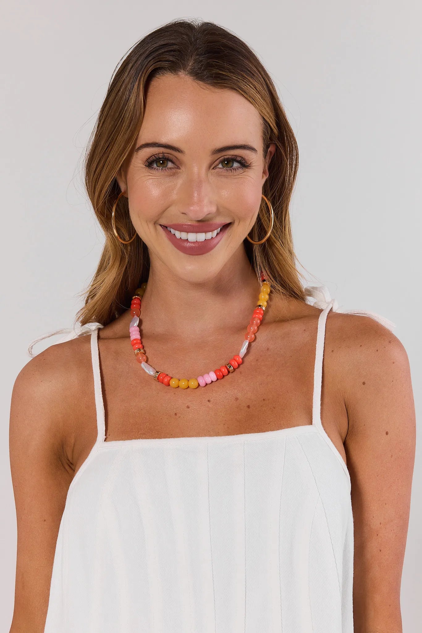 Woman wearing a colorful beaded necklace and white top against a plain background
