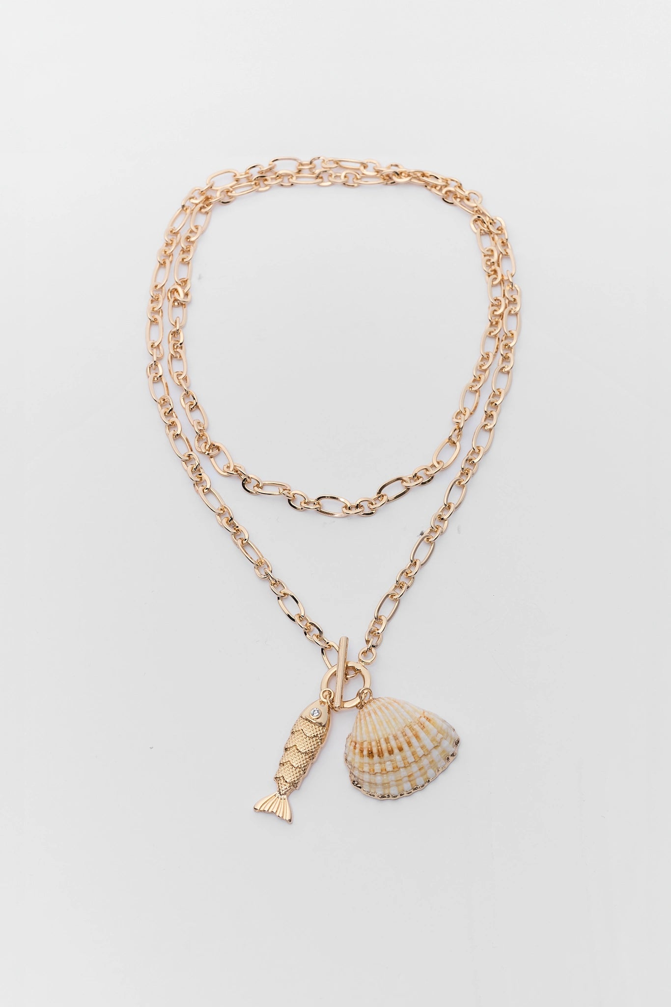 Gold necklace with shell and fish charm on a light gray background