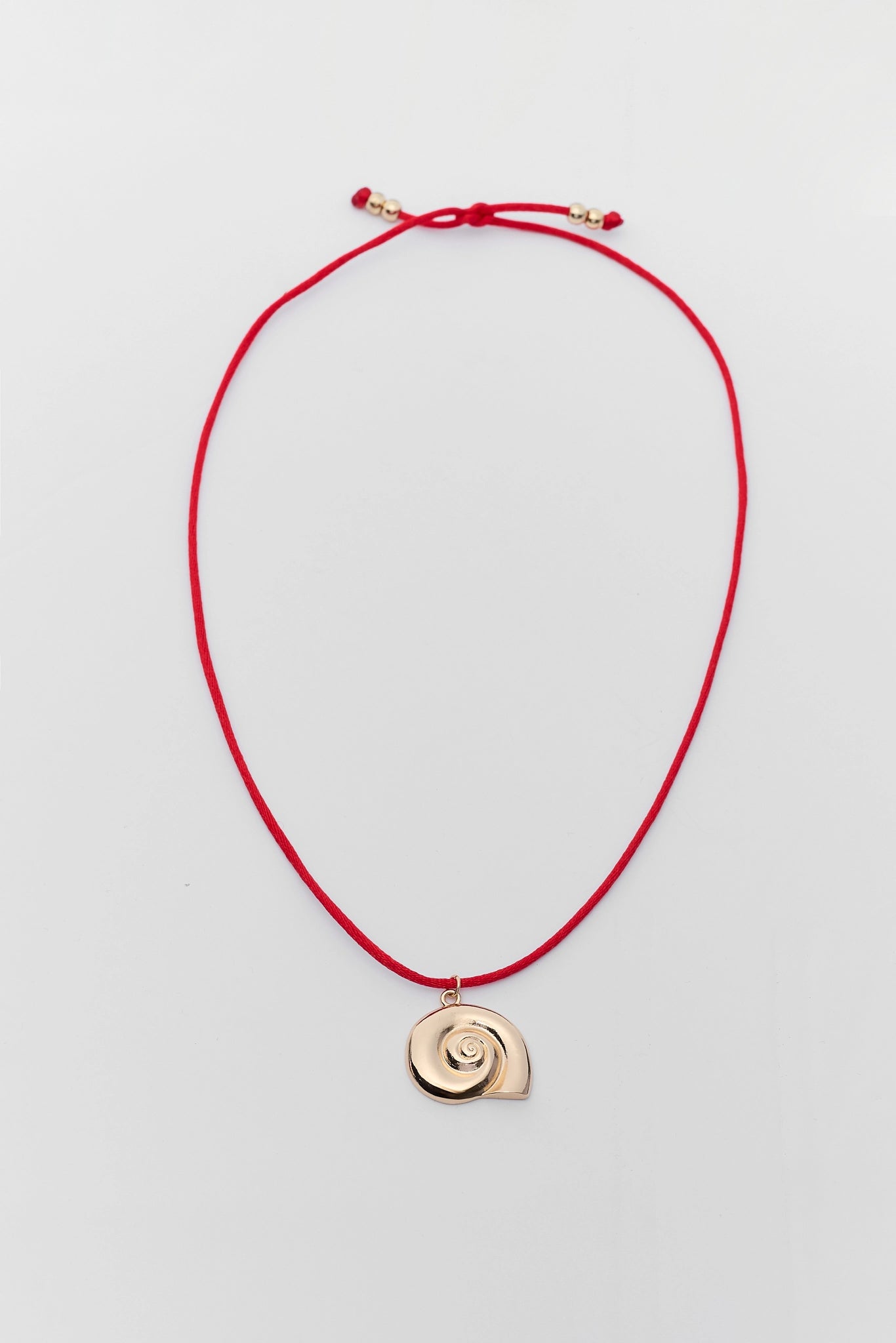 Red cord necklace with a gold shell pendant on a light gray background