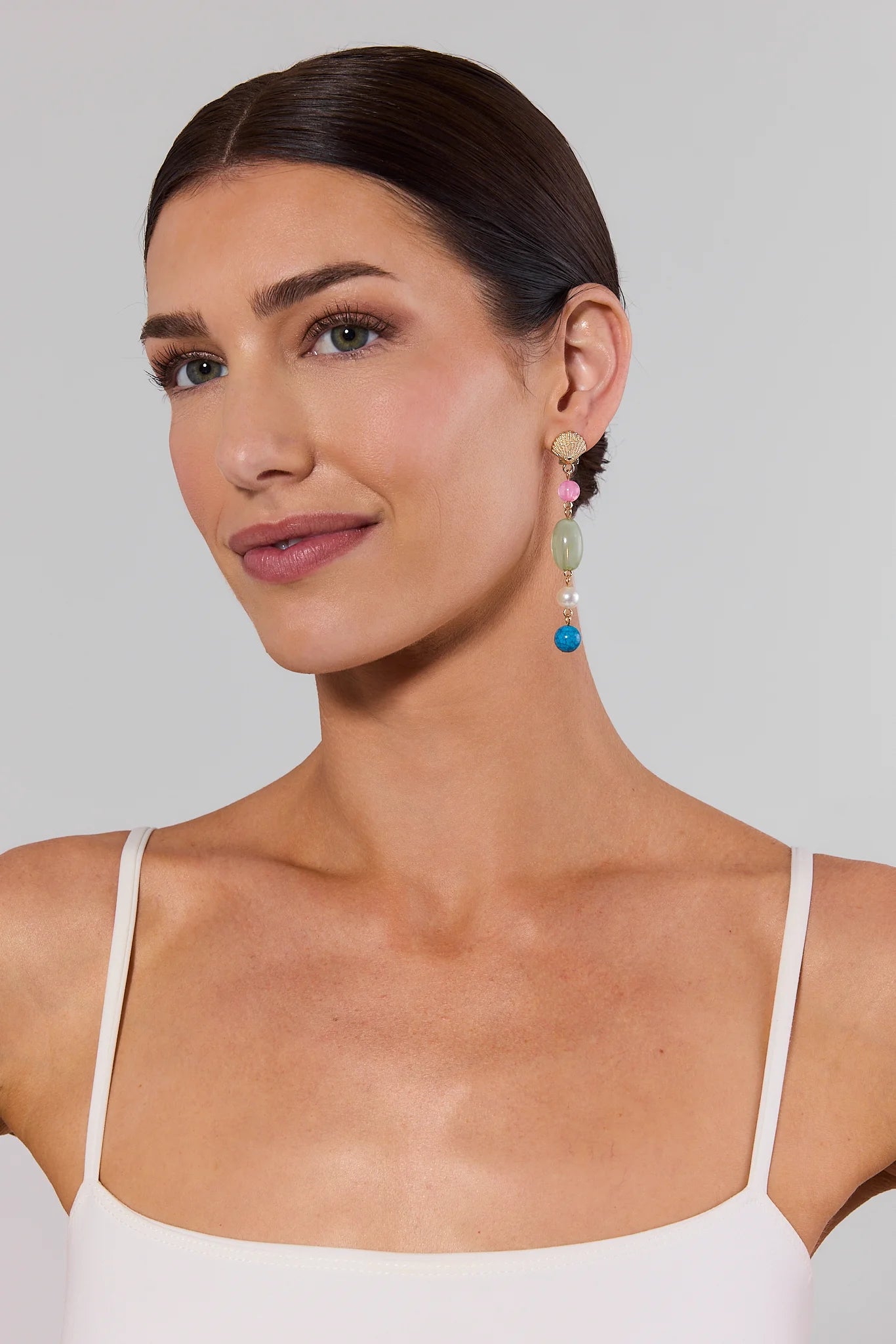 Woman wearing multi stone drop earrings against a plain background