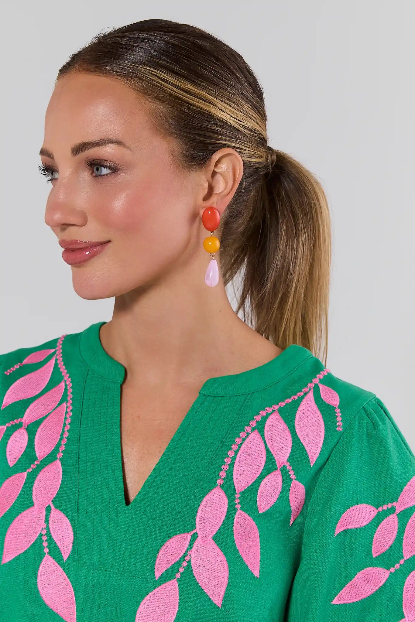 Woman wearing colorful earrings with a green top with pink leaf patterns.