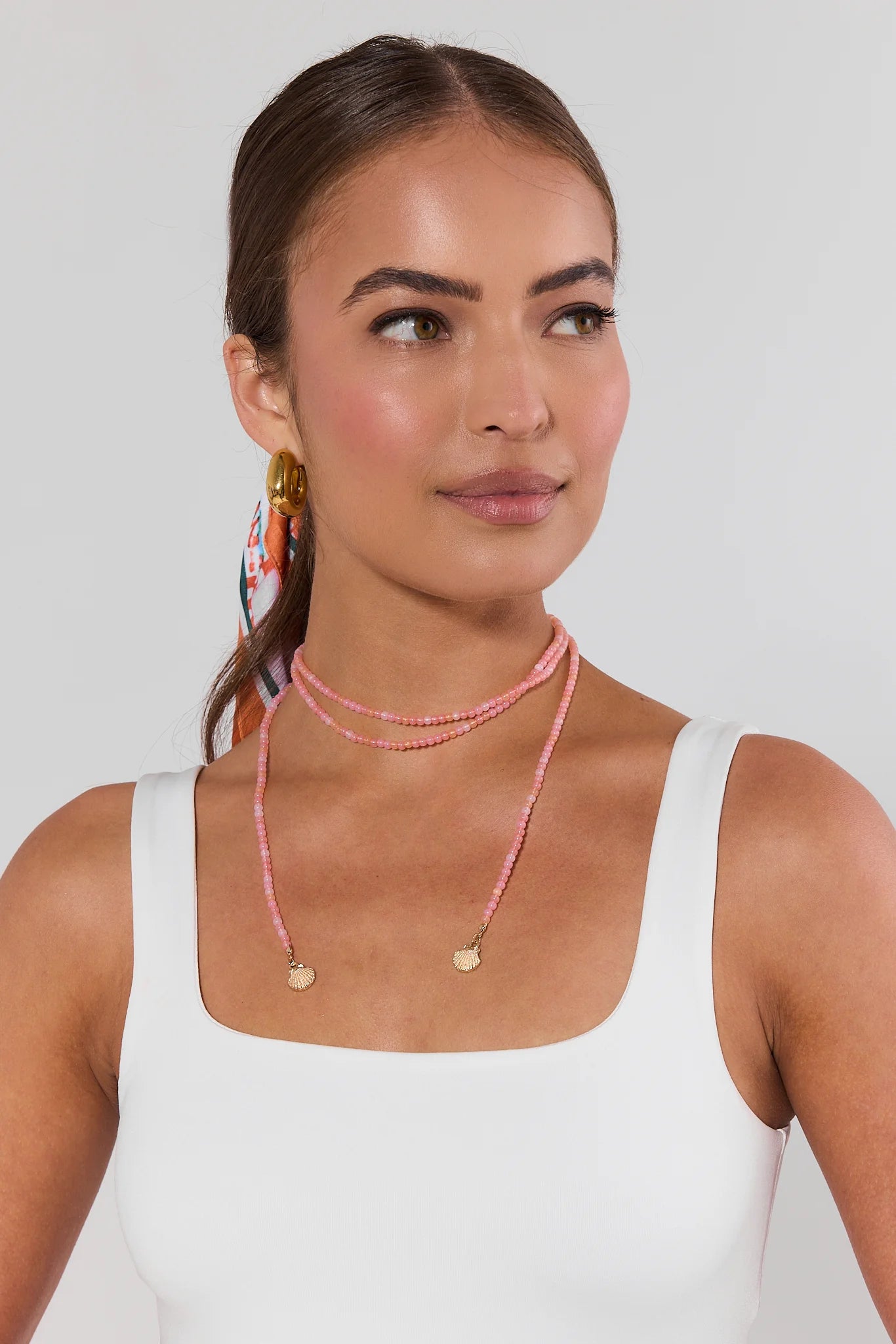 Woman wearing a white tank top and pink beaded necklaces against a plain background