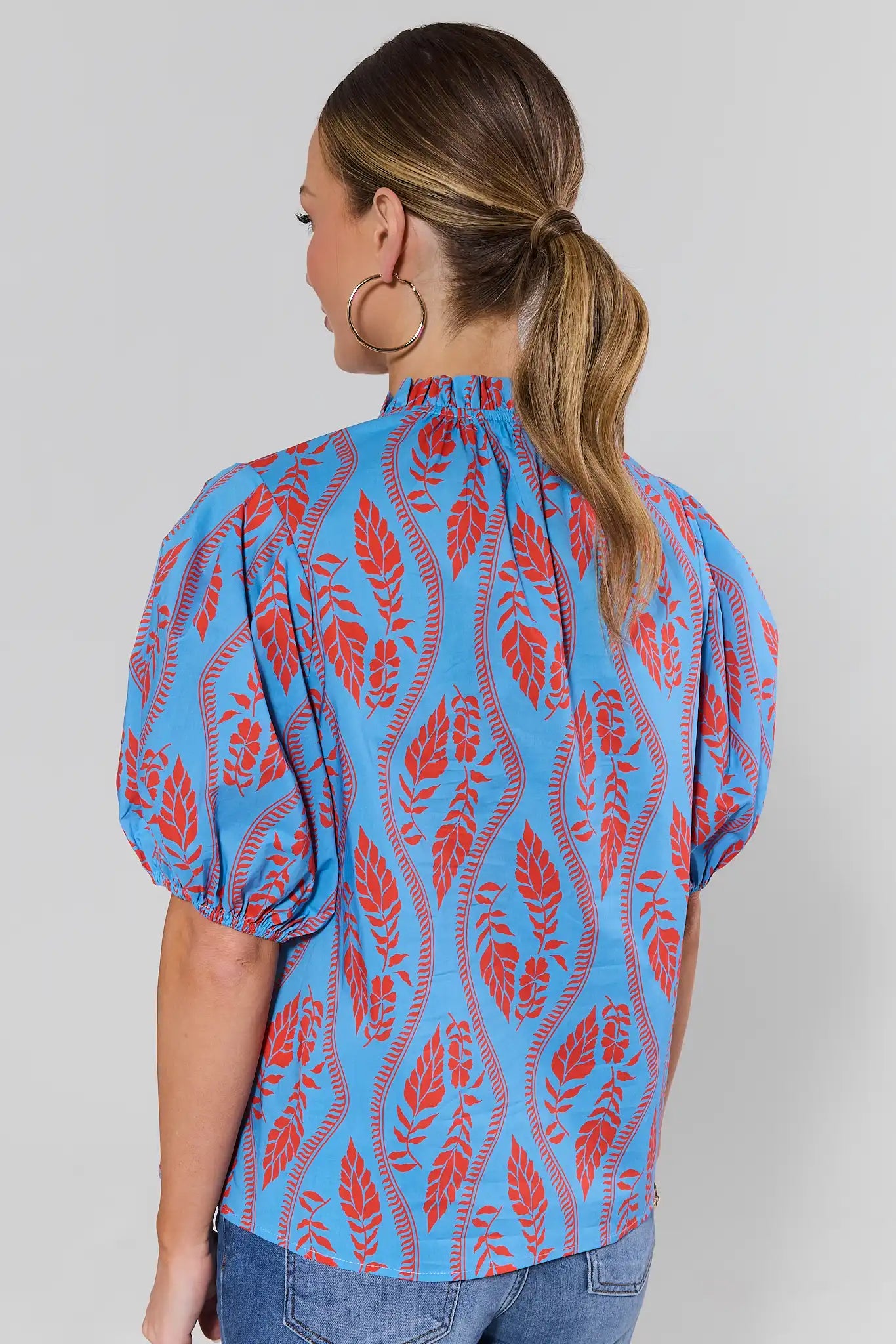 Woman standing wearing a blue blouse with red leaf pattern on a plain background