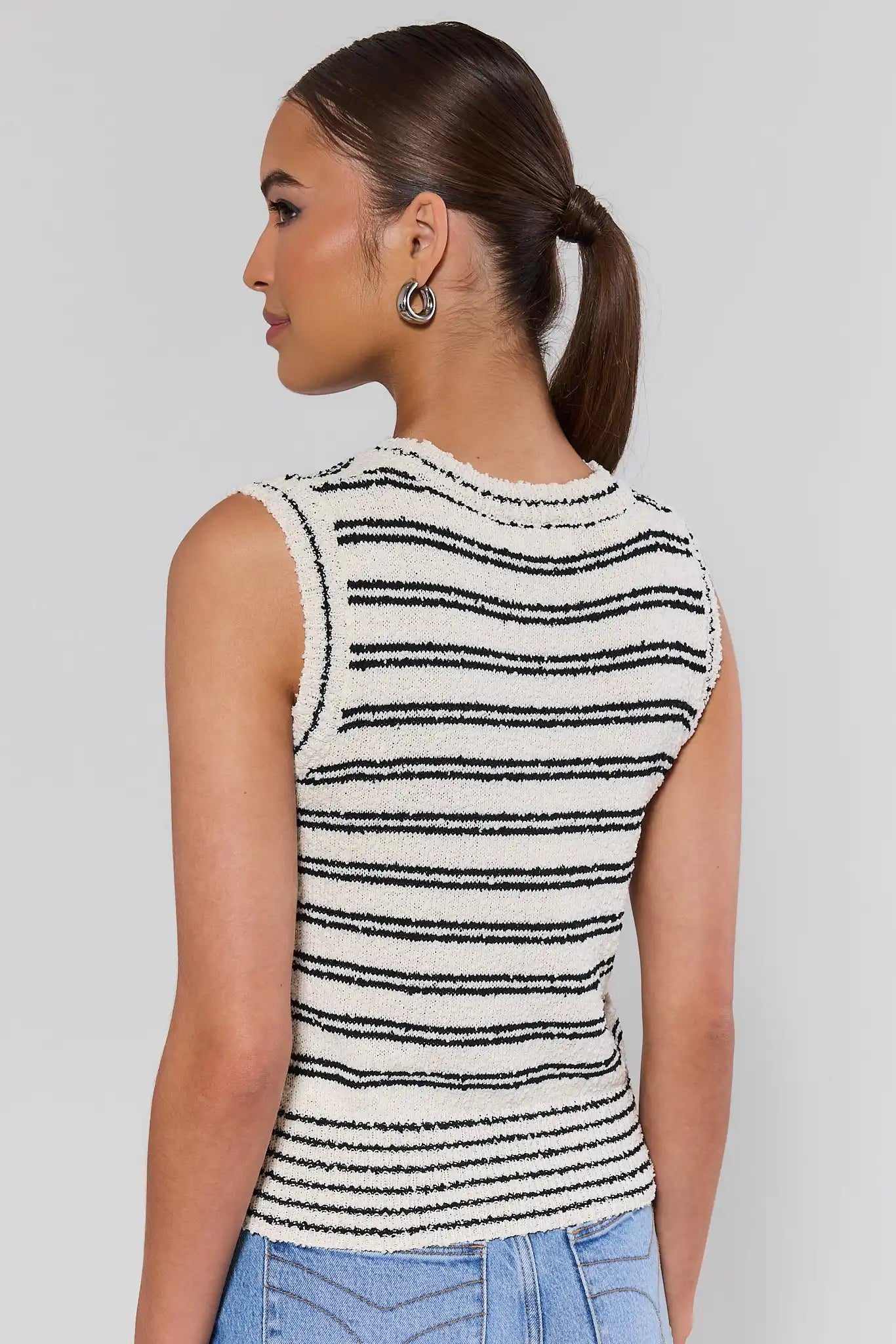Woman standing wearing a sleeveless black and white striped top against a plain background