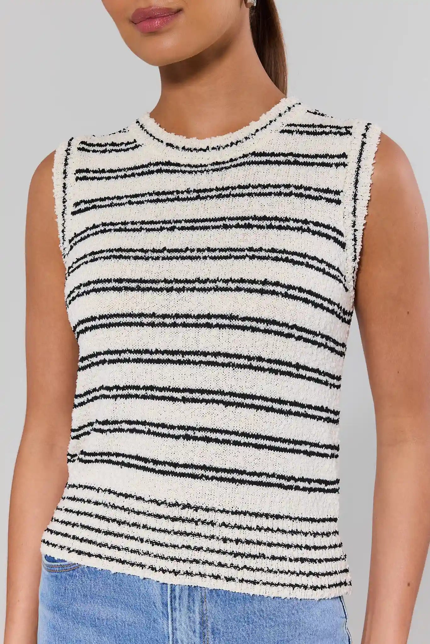 close up Person wearing a sleeveless black and white striped top with a plain background