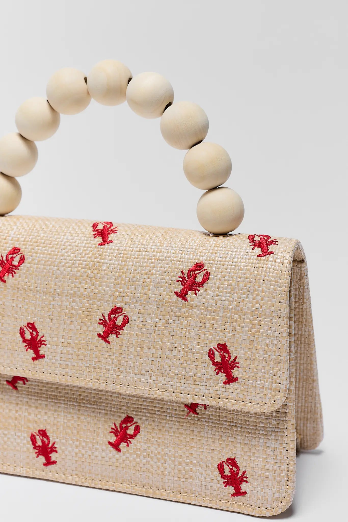 close up Beige handbag with red lobster patterns and wooden bead handle on a light gray background