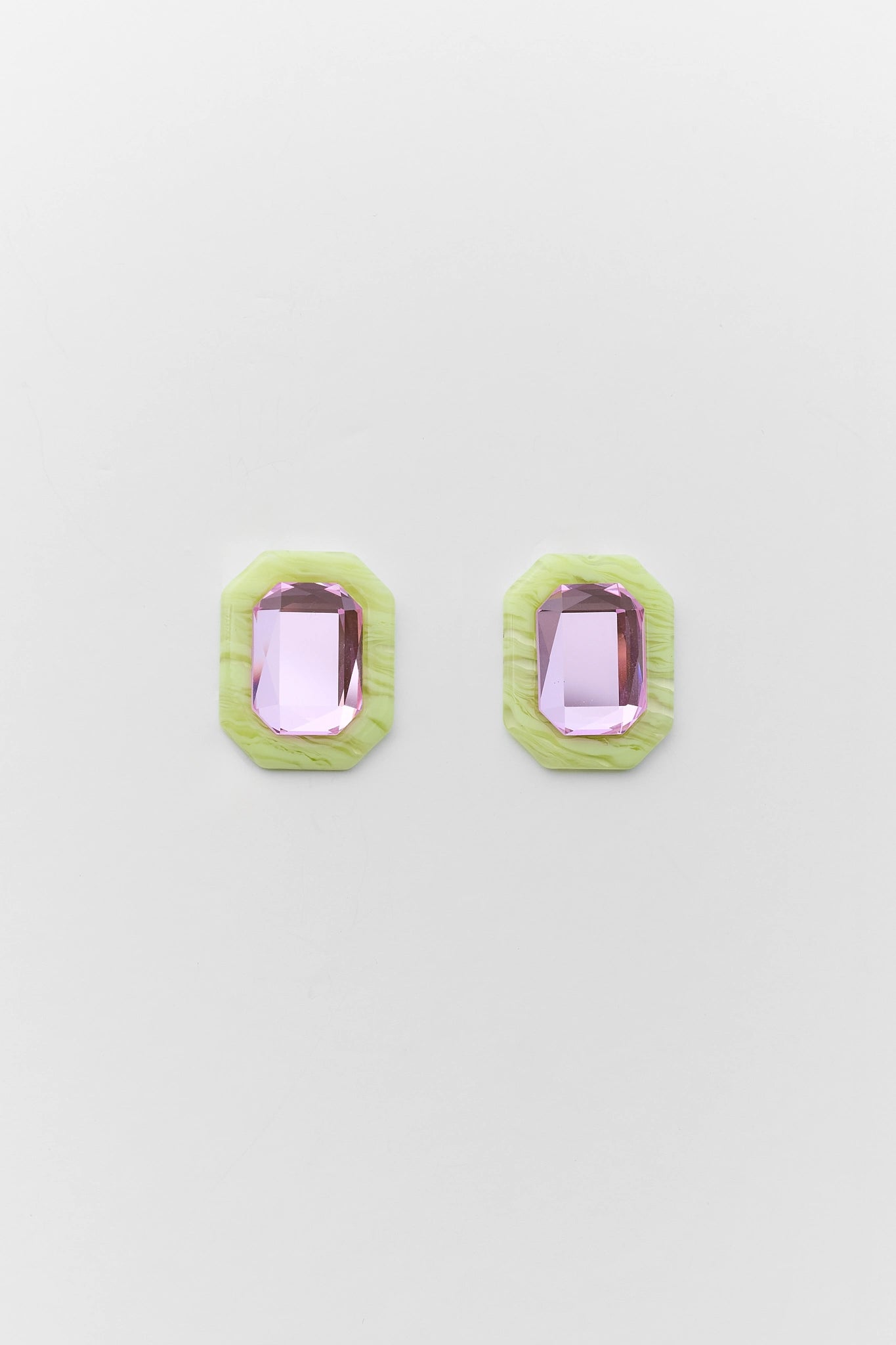 Pair of earrings with green frame and pink gemstones on a light gray background