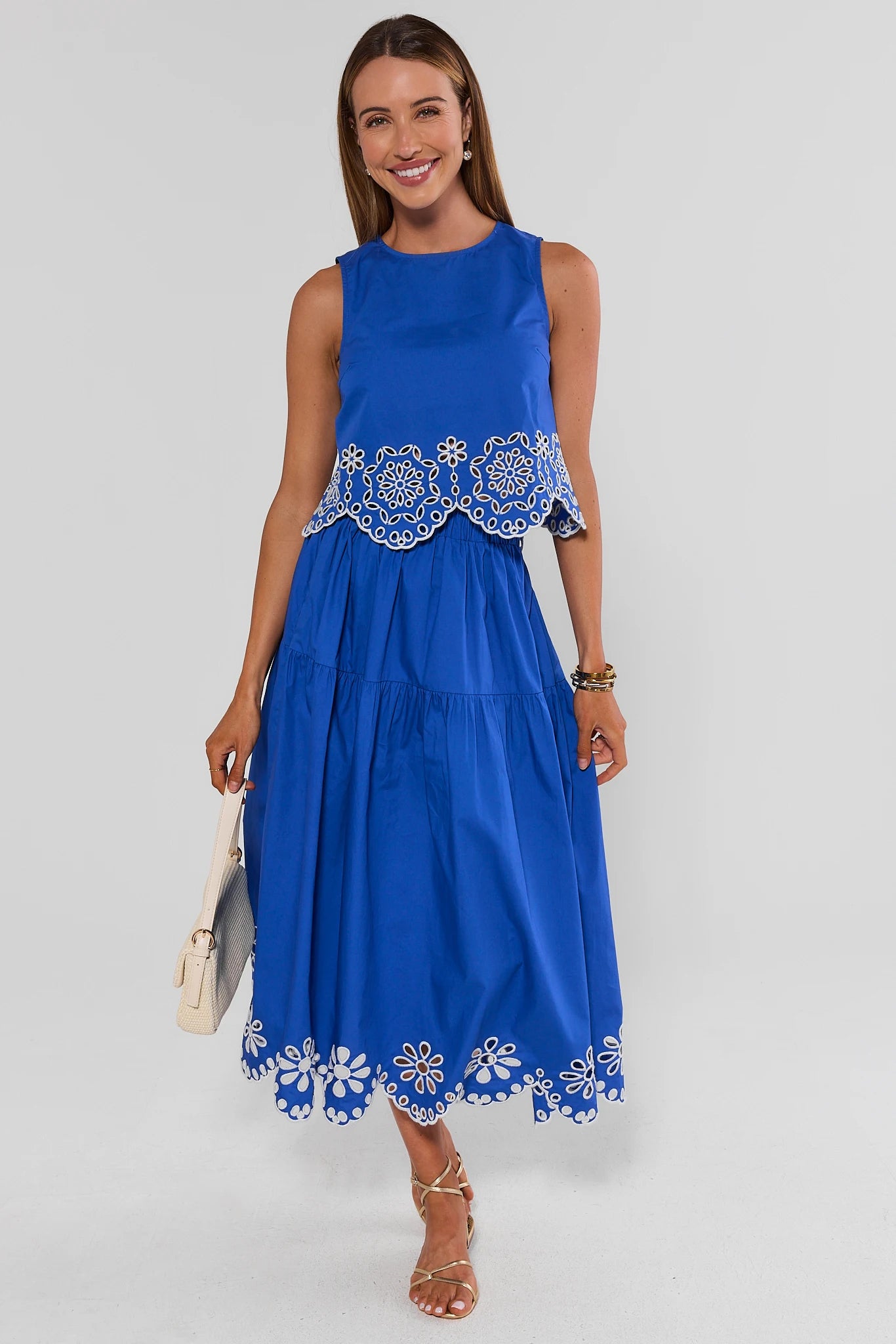 Woman wearing a blue dress with white embroidery on a gray background standing