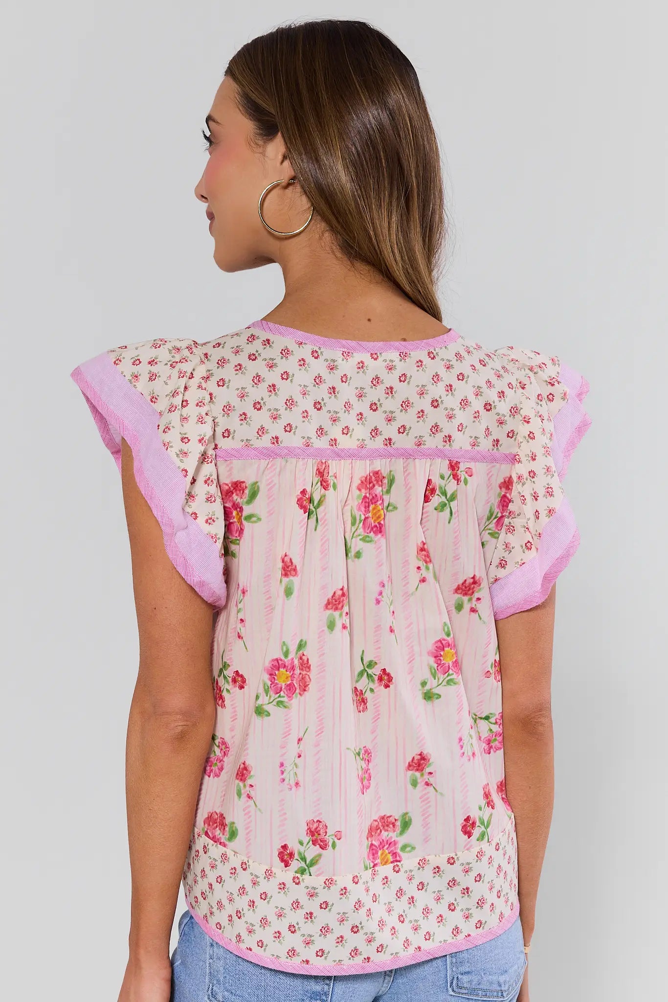 Woman standing wearing a floral blouse with pink trim on a plain background
