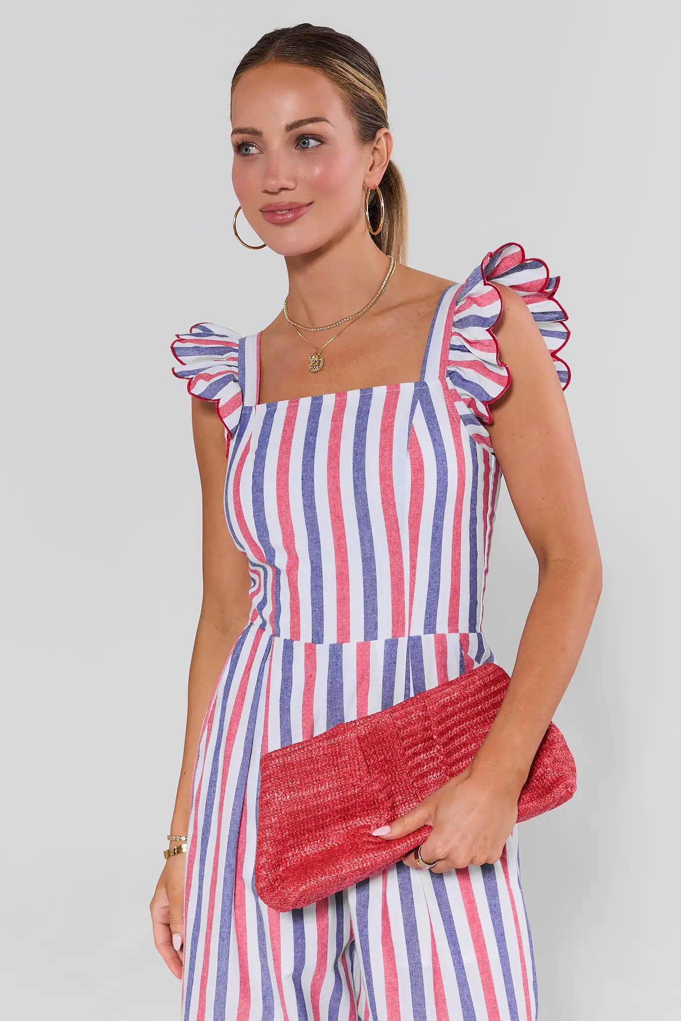 Woman wearing a striped dress with ruffled sleeves and holding a red clutch against a plain background