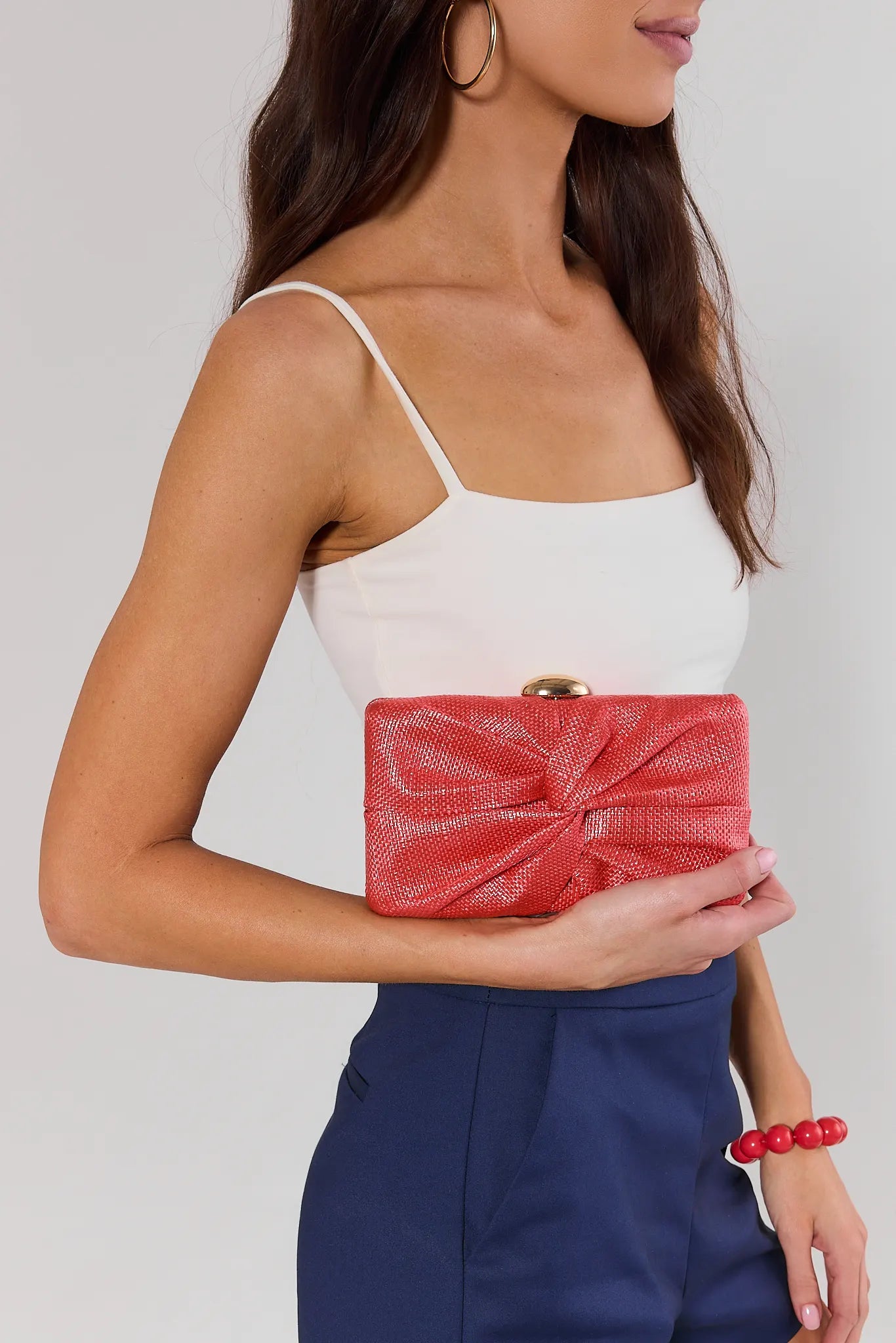 Woman holding a red clutch against a plain background