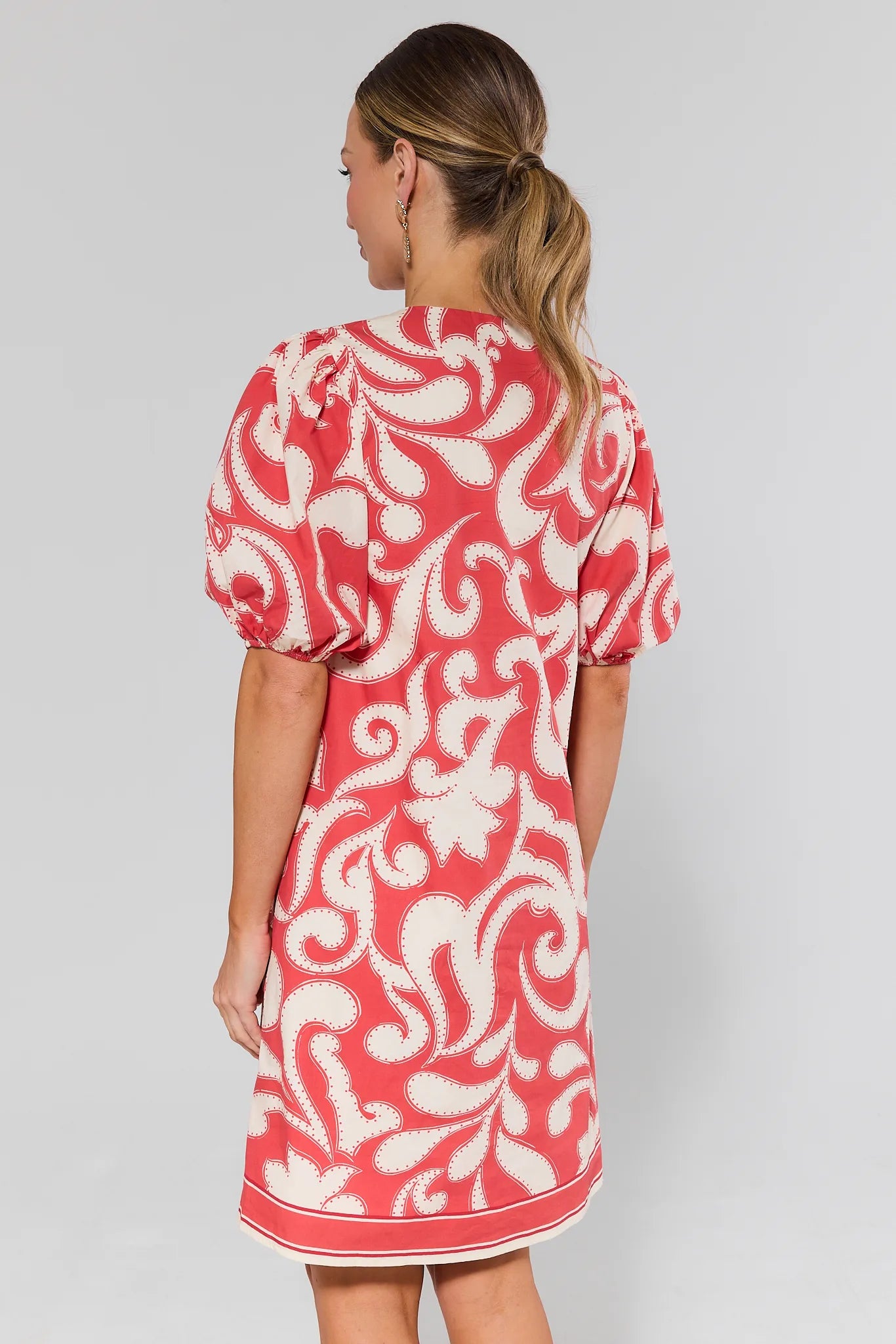 Woman standing wearing a red and white patterned dress on a plain background