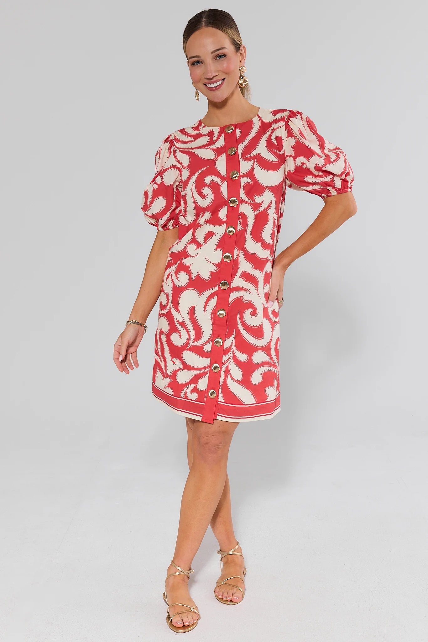 Woman wearing a red and white patterned dress and flats on a gray background