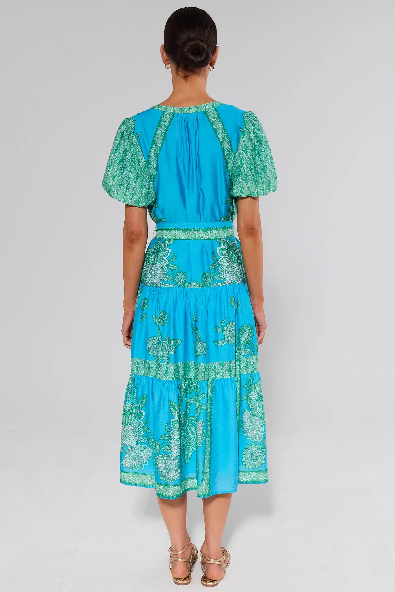 Woman standing wearing a turquoise dress with green patterns on a white background