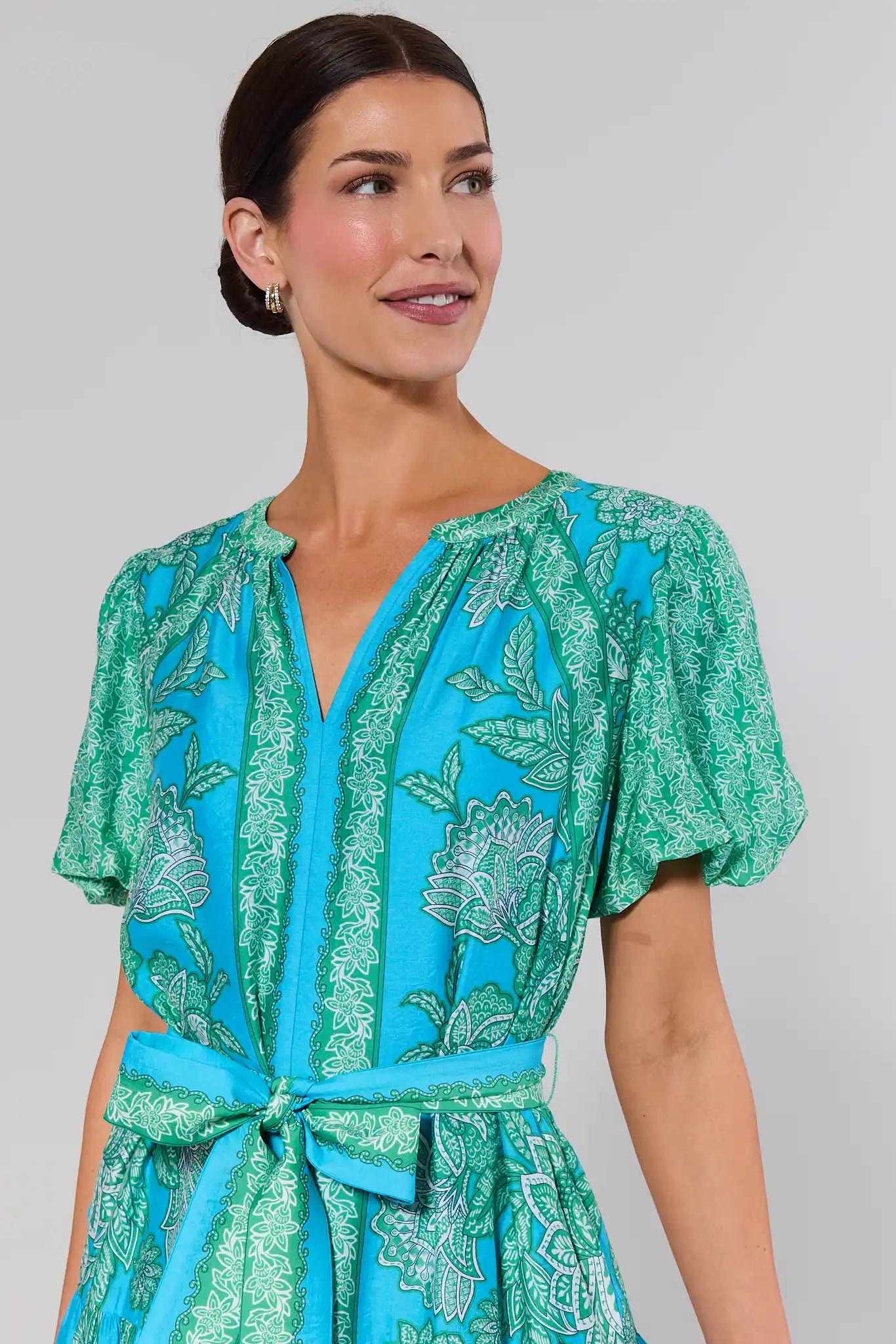 close up Woman wearing a green and blue patterned dress against a gray background