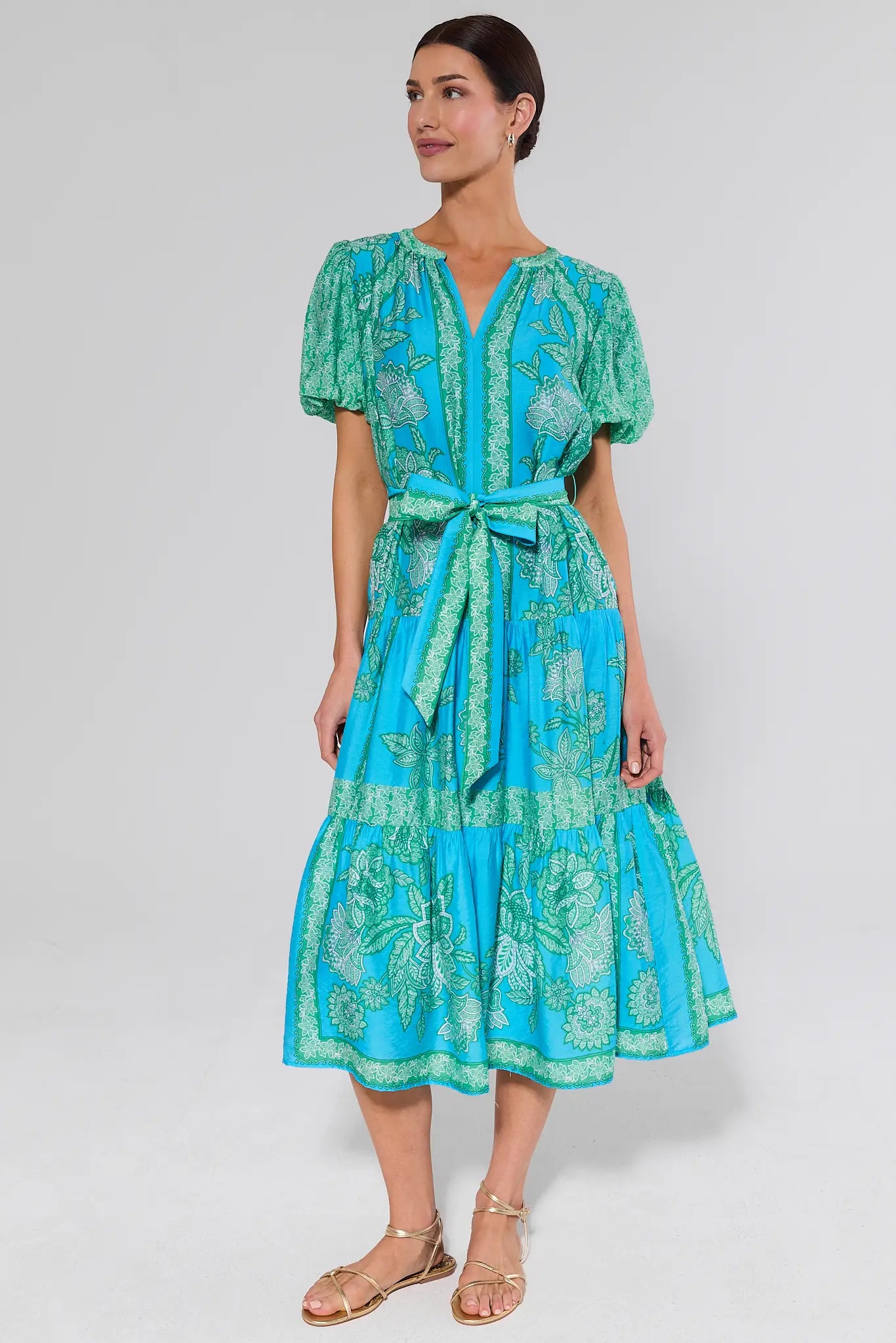 Woman wearing a blue and green split neck patterned dress on a white background