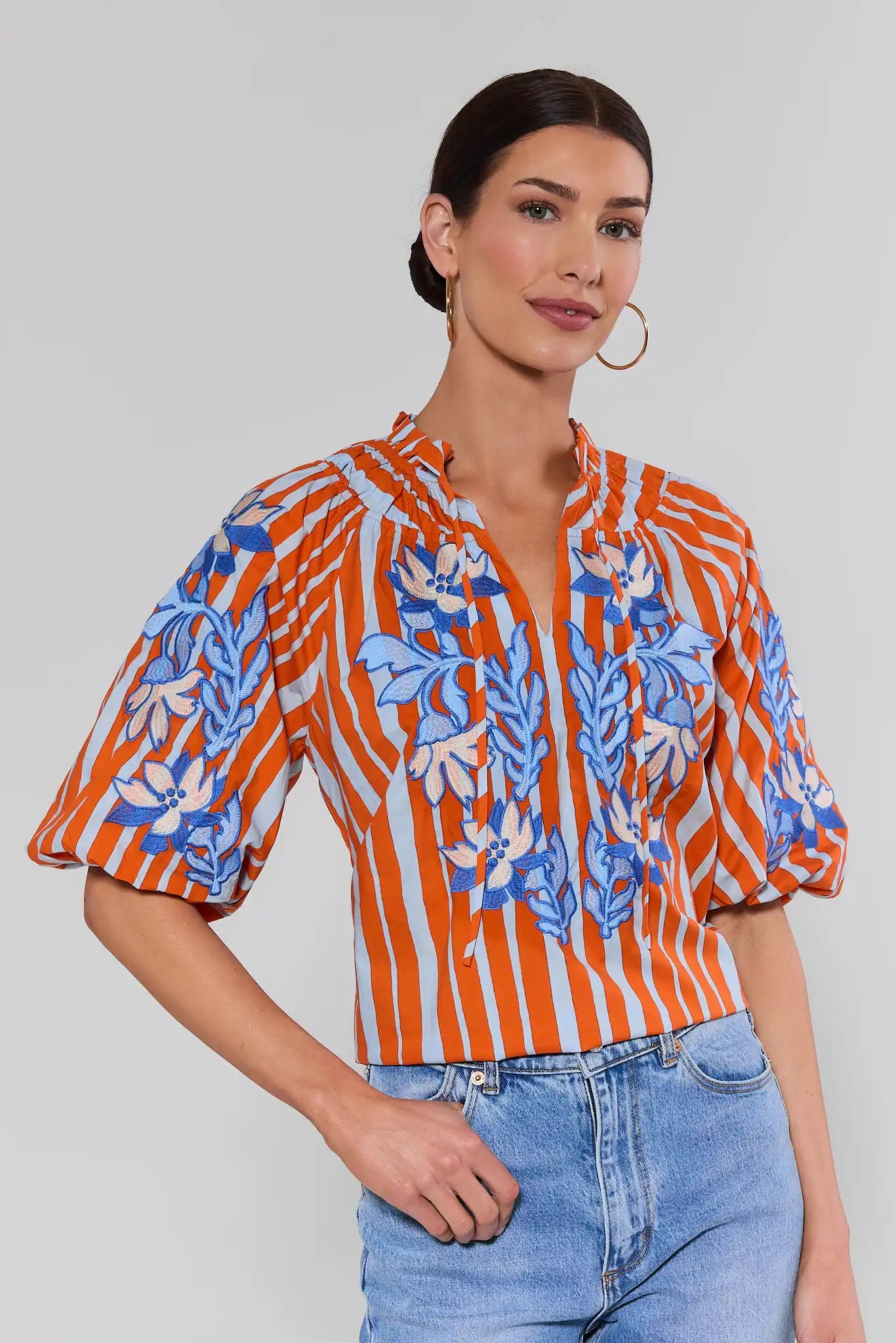 Woman wearing an orange and blue patterned blouse with a plain background