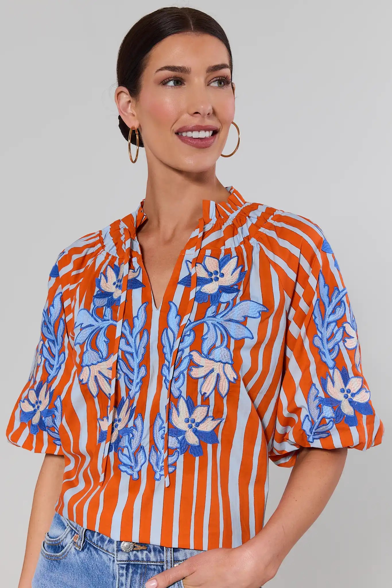 close up Woman wearing an orange and blue patterned blouse against a gray background