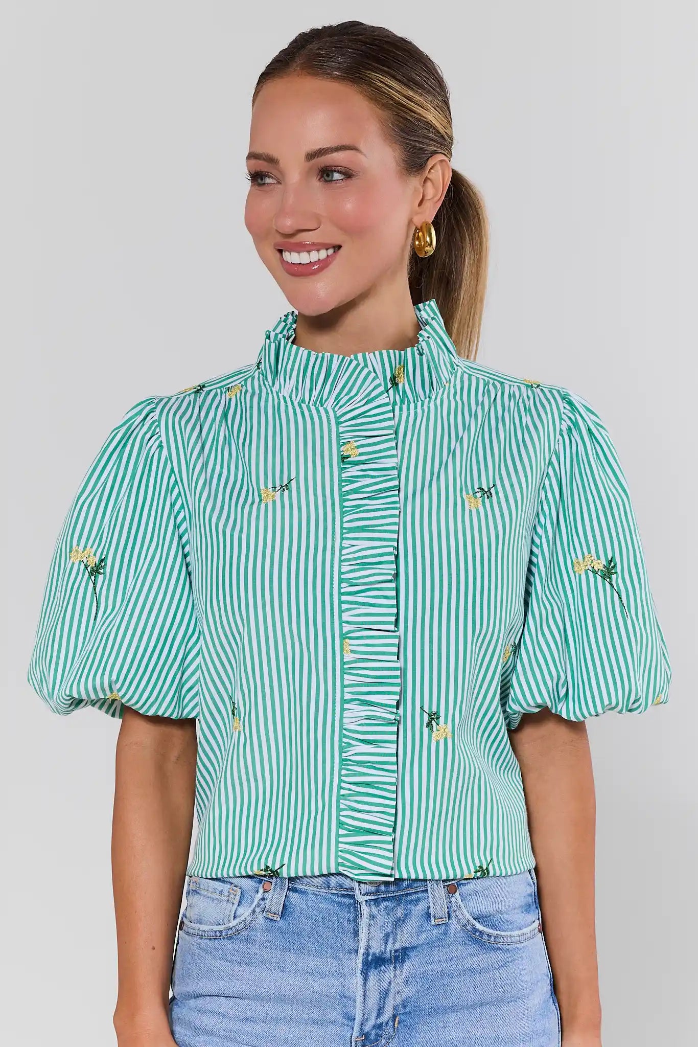 Woman wearing a green and white striped blouse with floral details on a plain background