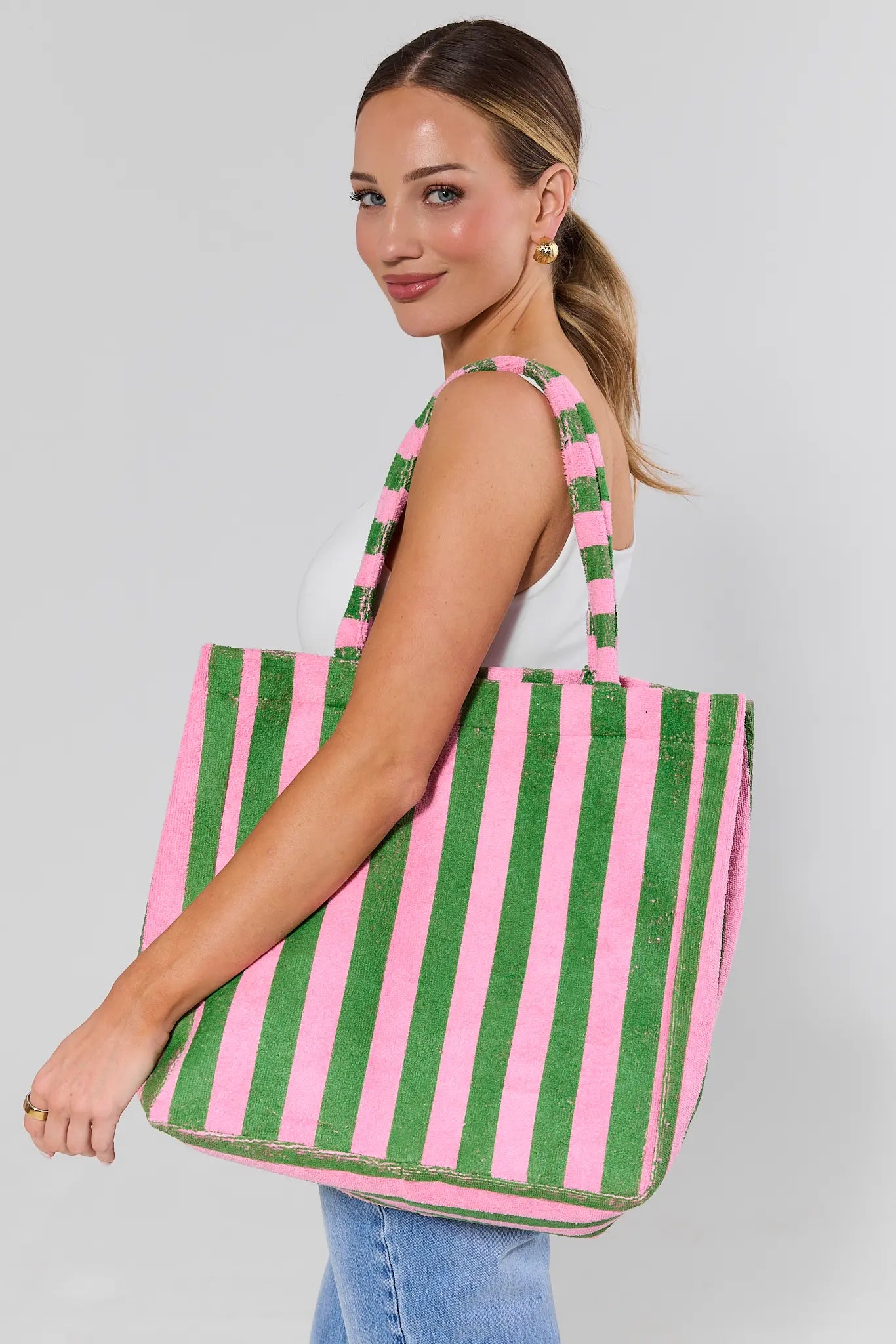 Woman holding a green and pink striped tote bag against a gray background