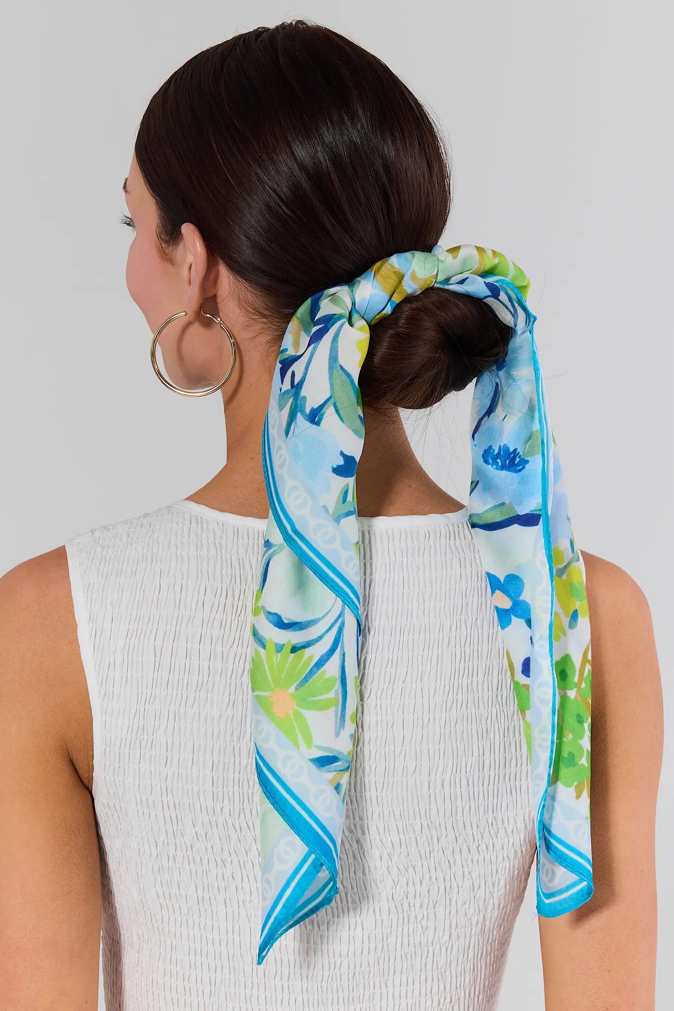 Woman with a floral scarf tied around her hair against a plain background