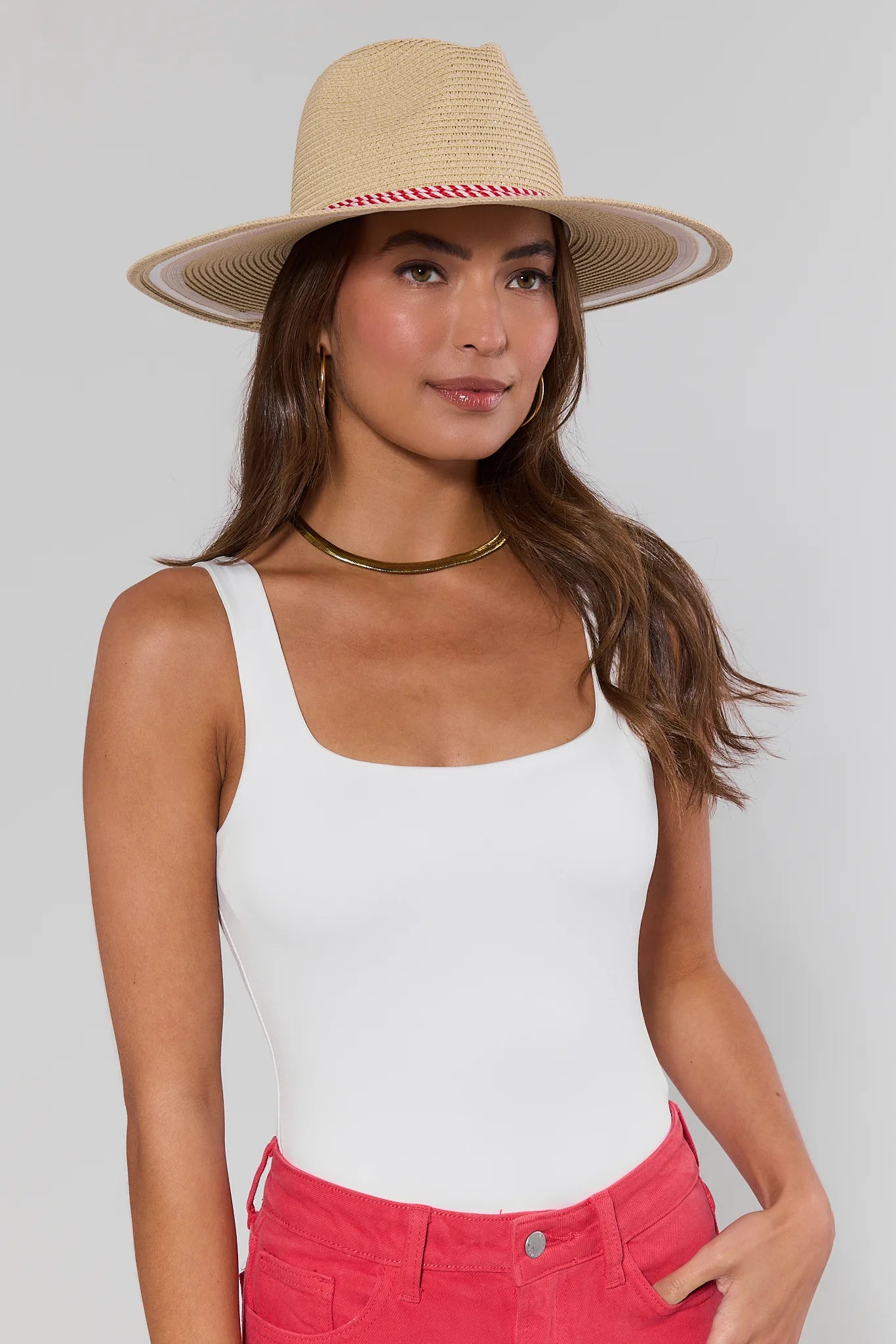 Woman wearing a straw hat, white tank top, and pink pants on a plain background