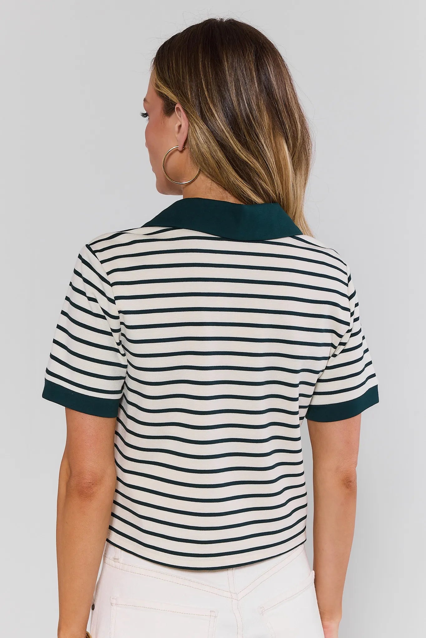 Woman standing wearing a striped polo shirt with green trim on a plain background
