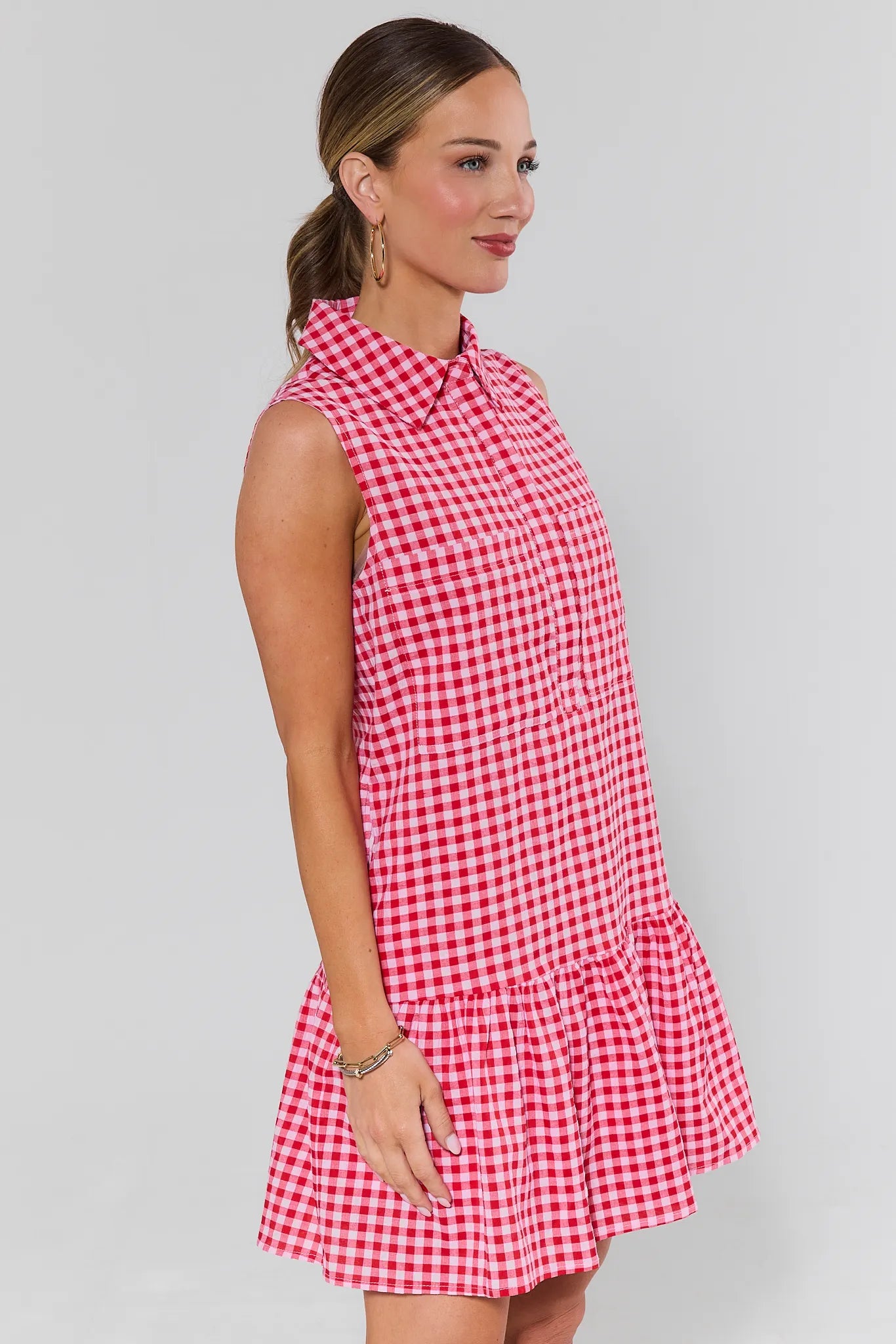 side shot Woman wearing a red and white checkered dress against a gray background