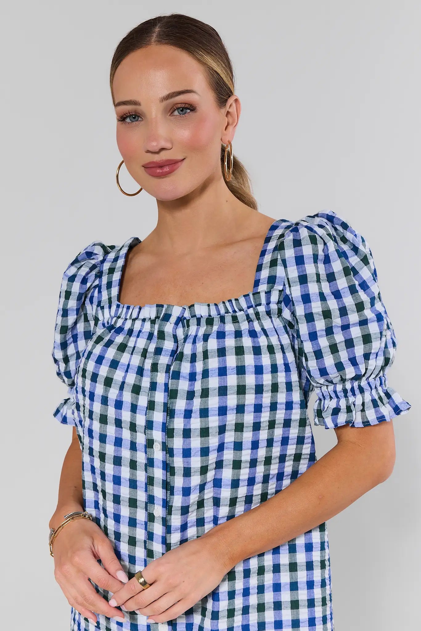 close up Woman wearing a blue and white checkered dress with puff sleeves against a plain background