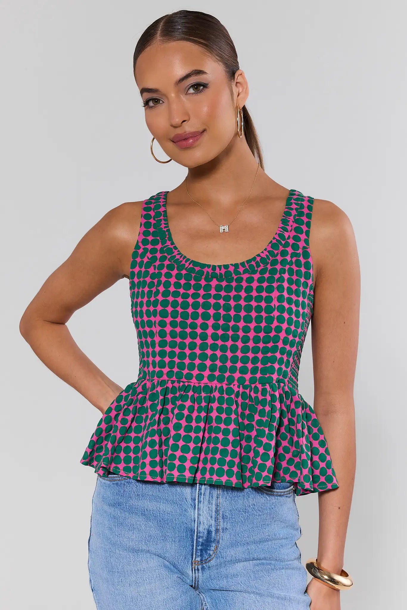 Woman wearing a green and pink checkered peplum top with blue jeans on a gray background