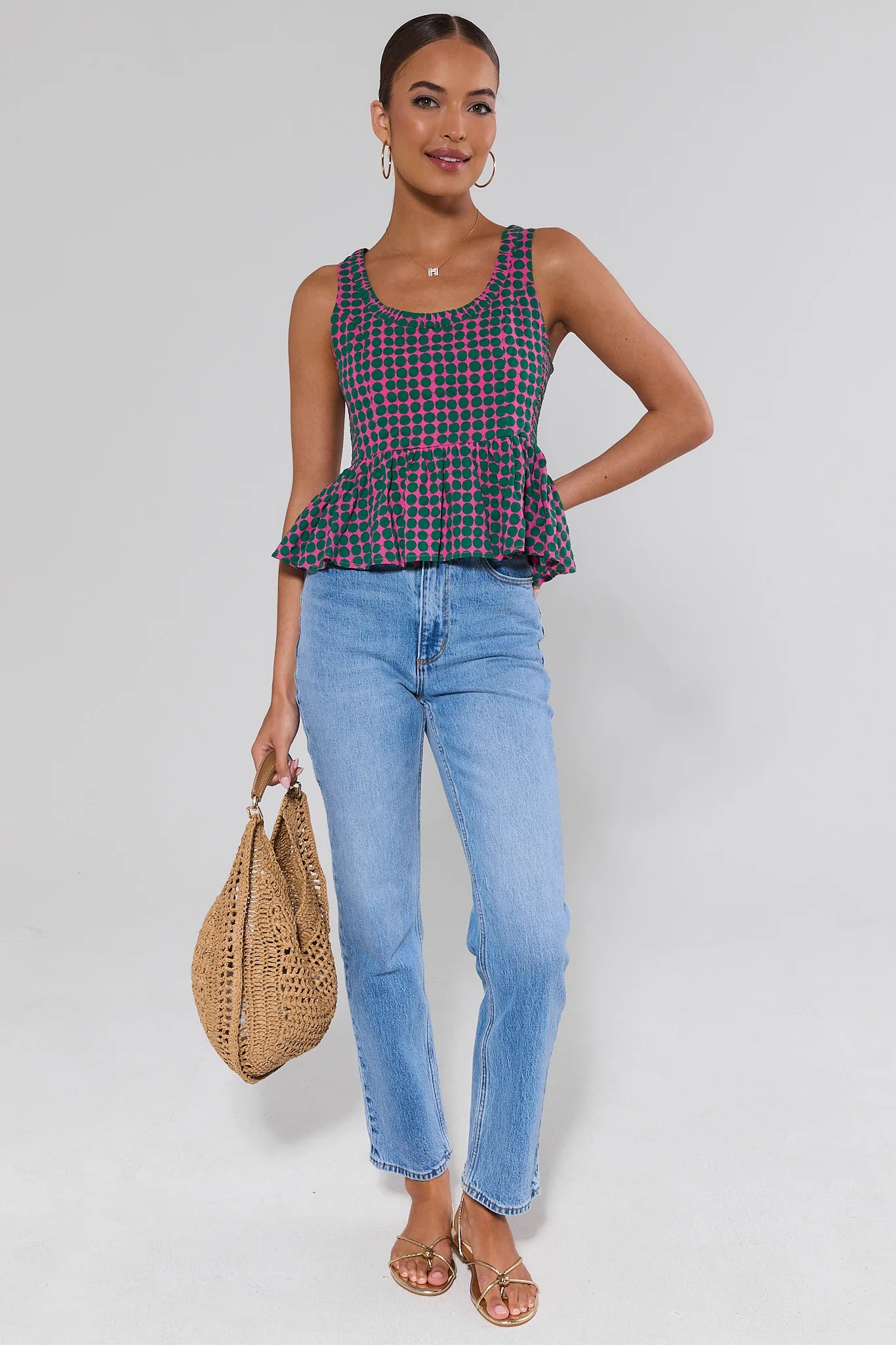 Woman wearing a plaid top and blue jeans, holding a woven bag on a plain background