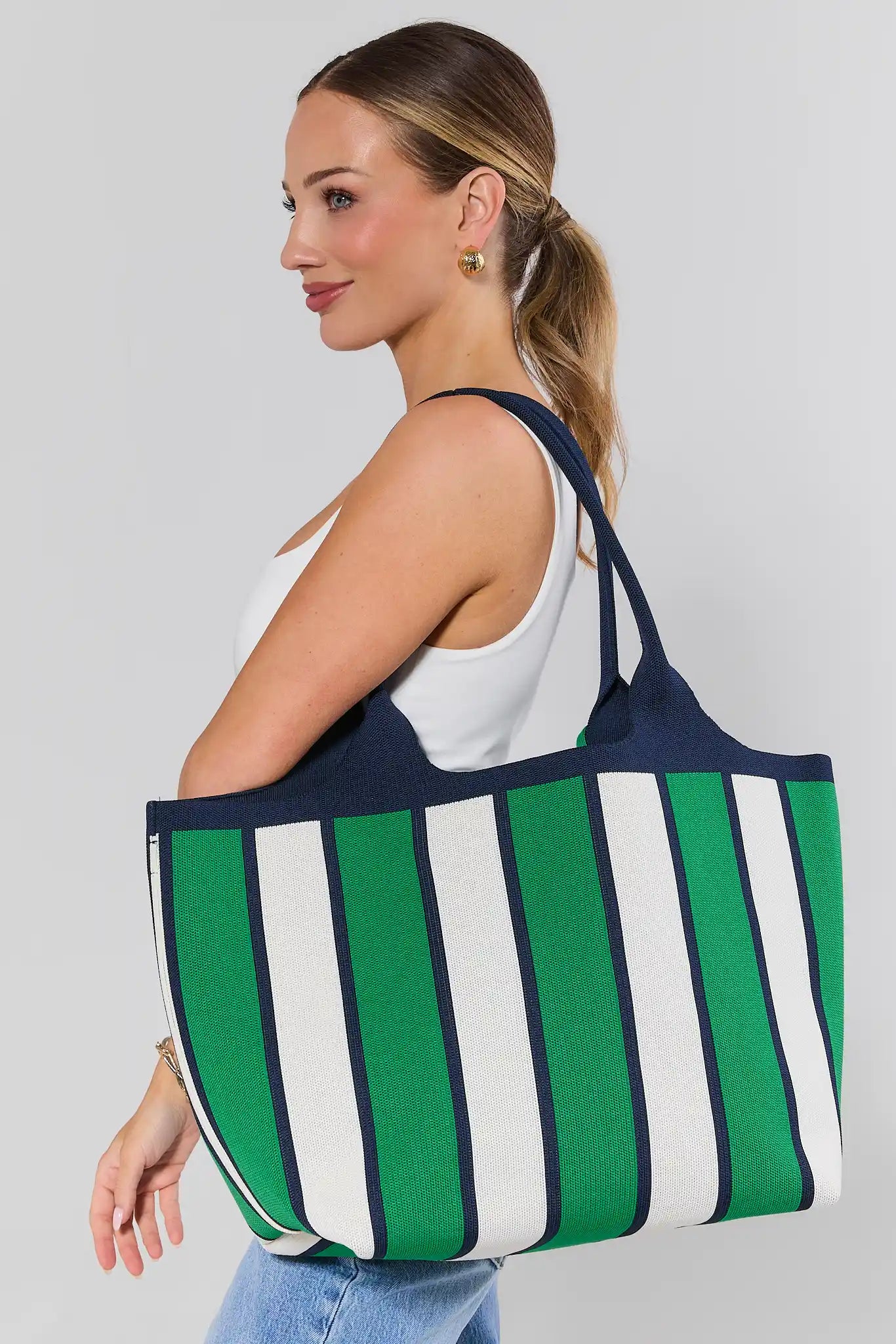 Woman carrying a green and white striped tote bag on a plain background