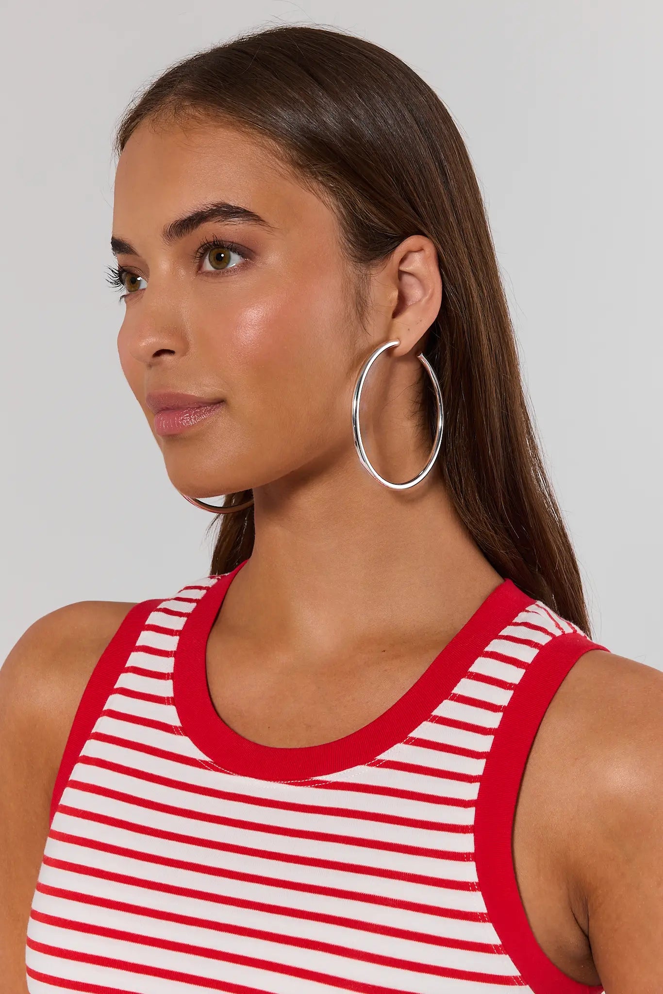 Woman wearing a red and white striped tank top with hoop earrings on a plain background