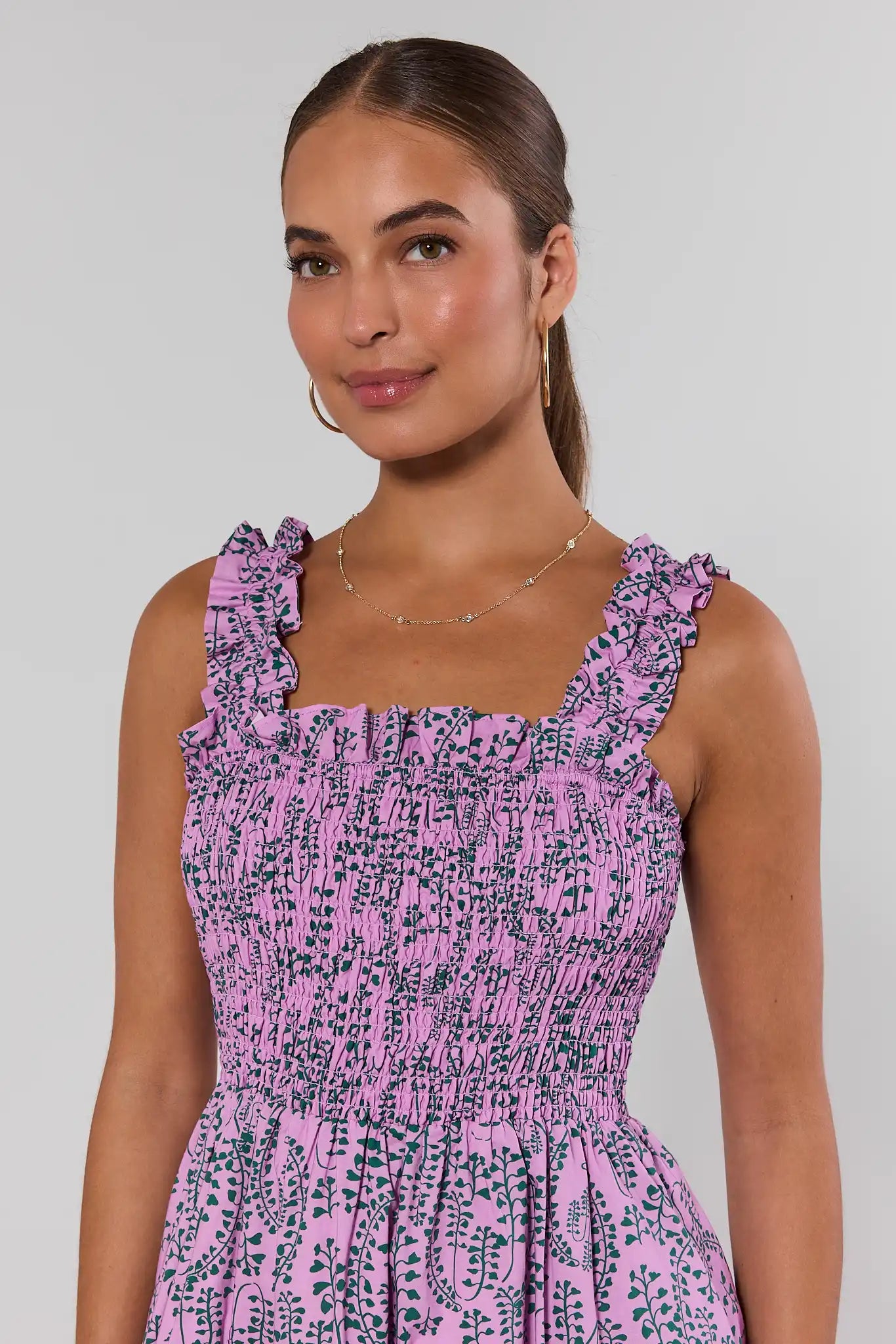 Woman wearing a pink and green smocked patterned dress against a gray background