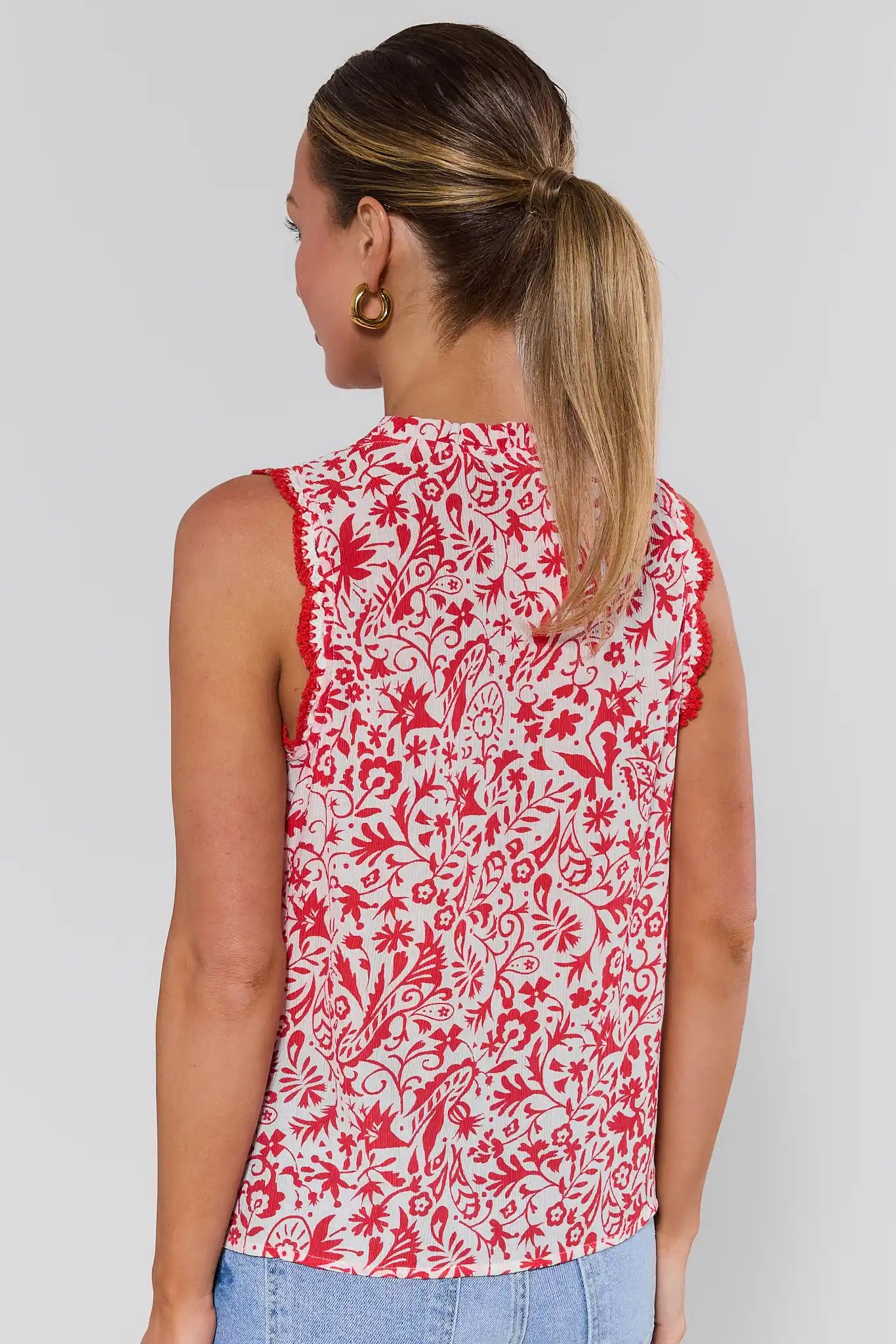 Woman standing wearing a red and white floral sleeveless top against a plain background