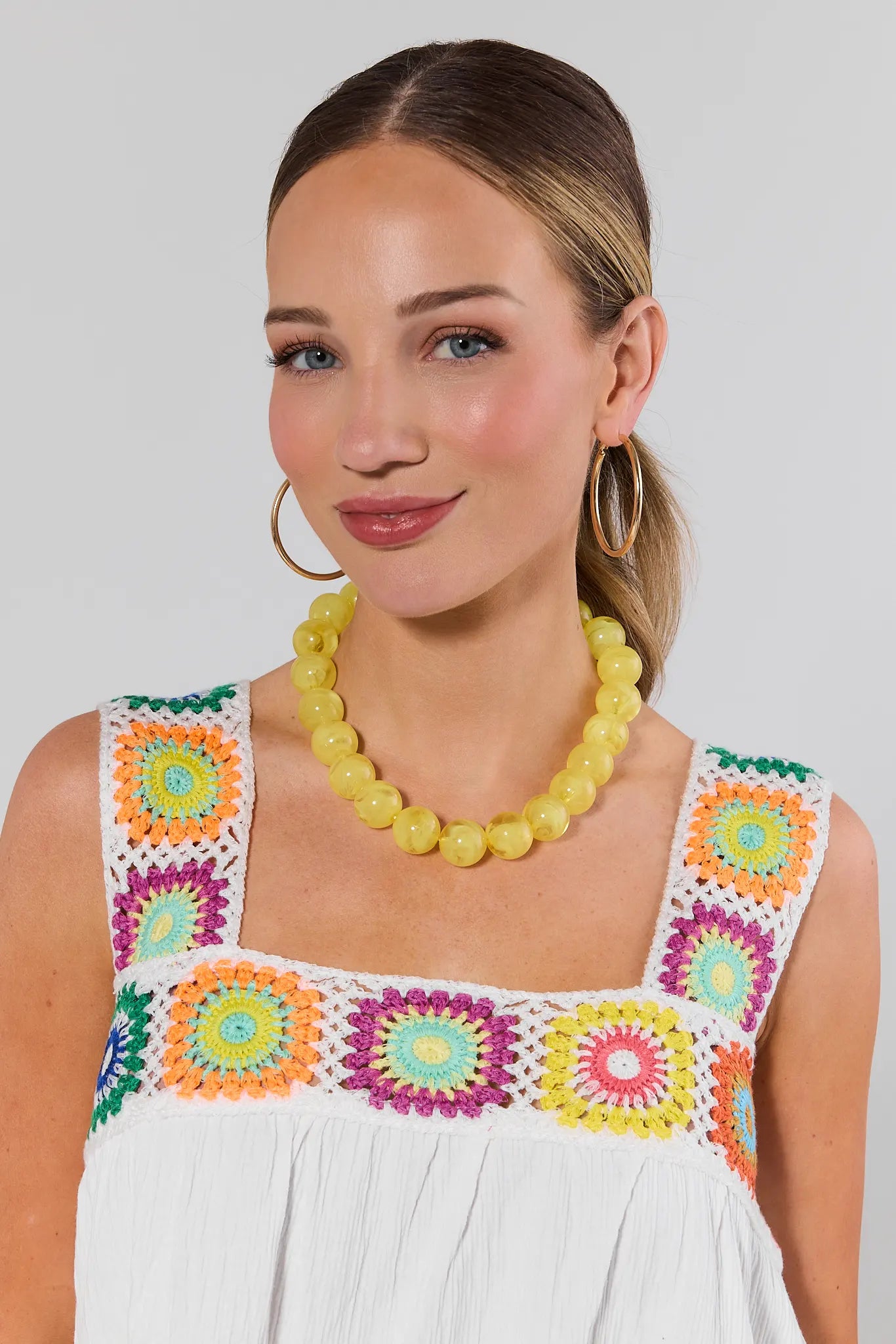 Woman wearing a colorful dress with floral patterns and a yellow necklace against a plain background