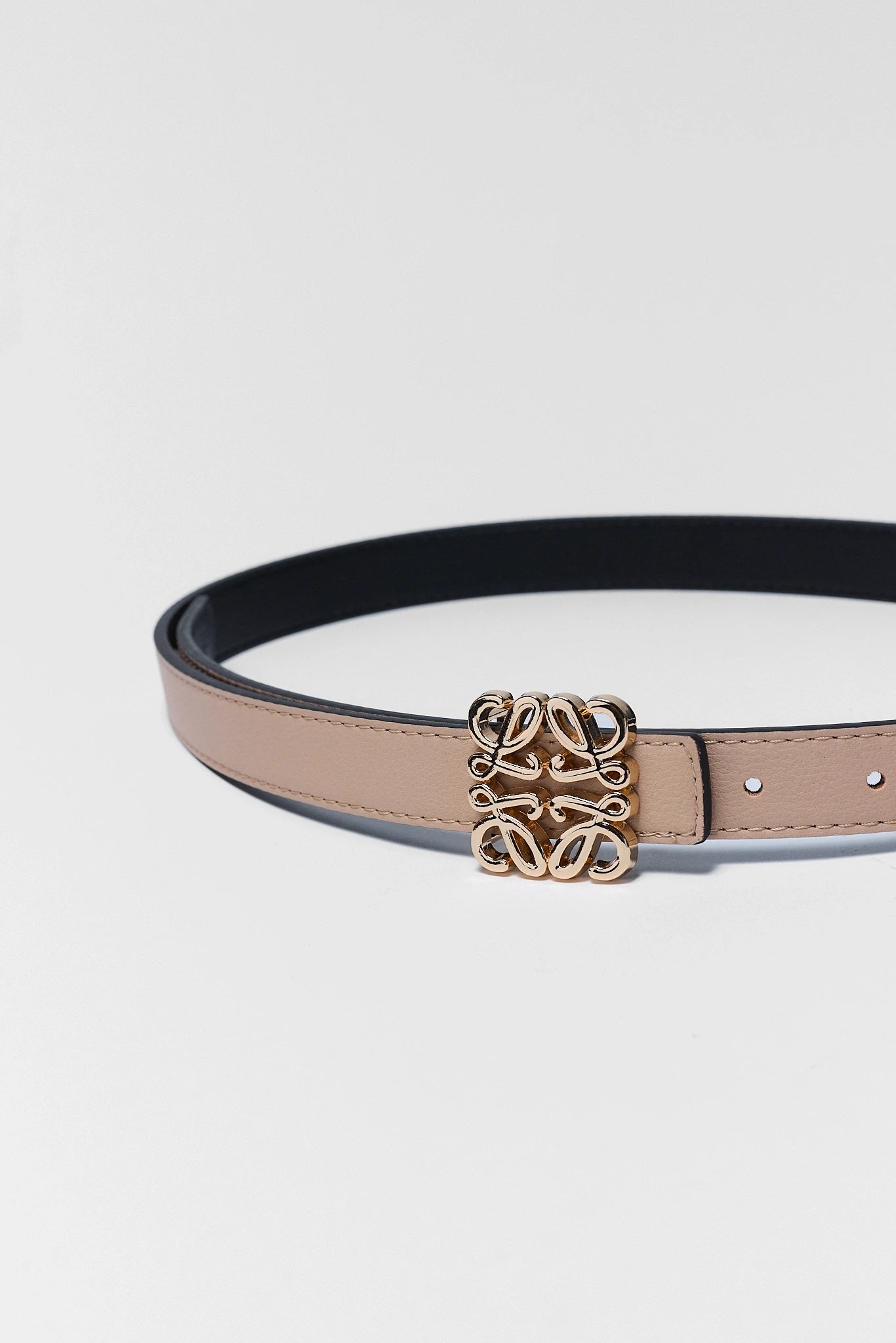close up Black belt with a beige strap and decorative gold buckle on a light gray background