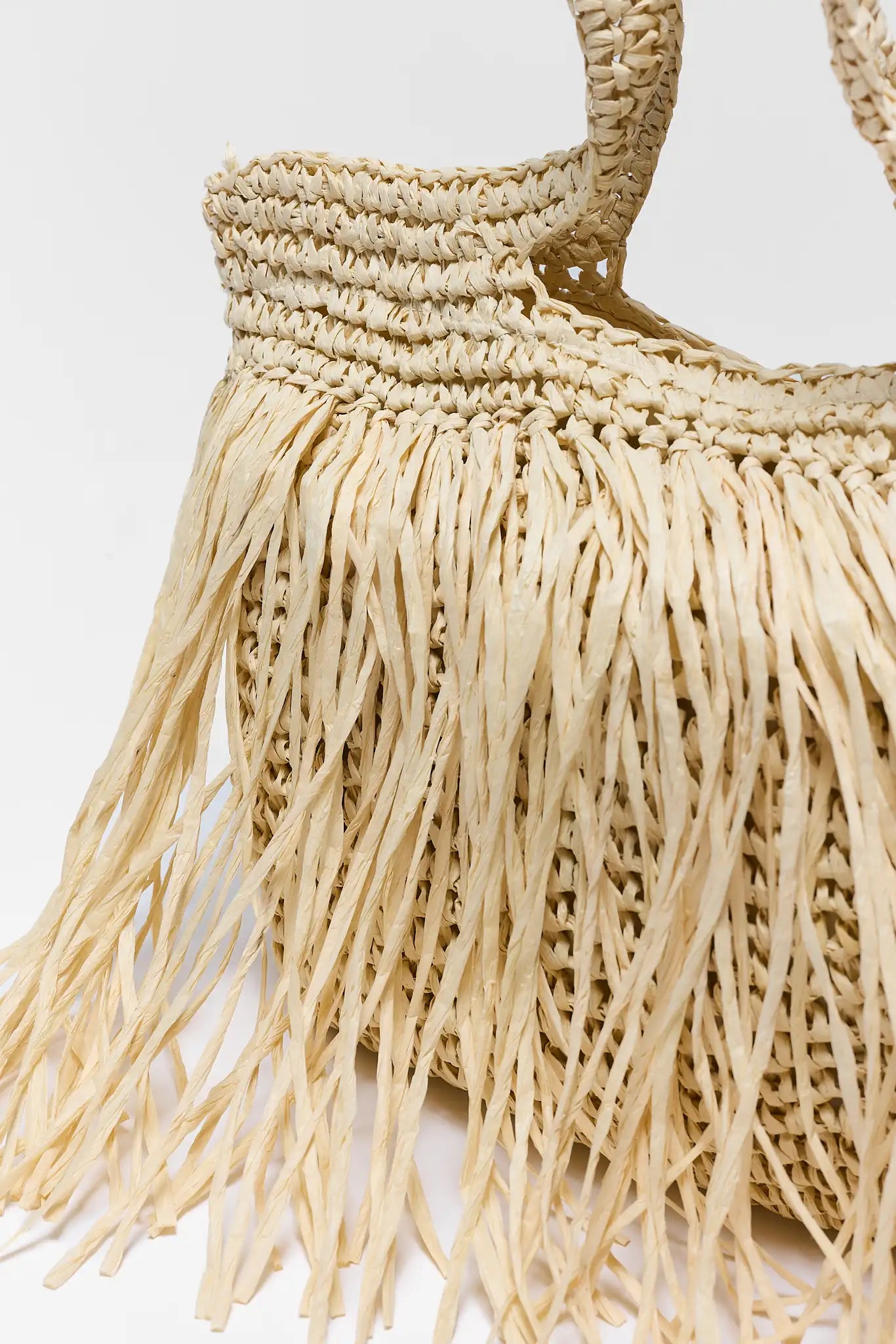 close up Beige woven handbag with fringe details on a light background