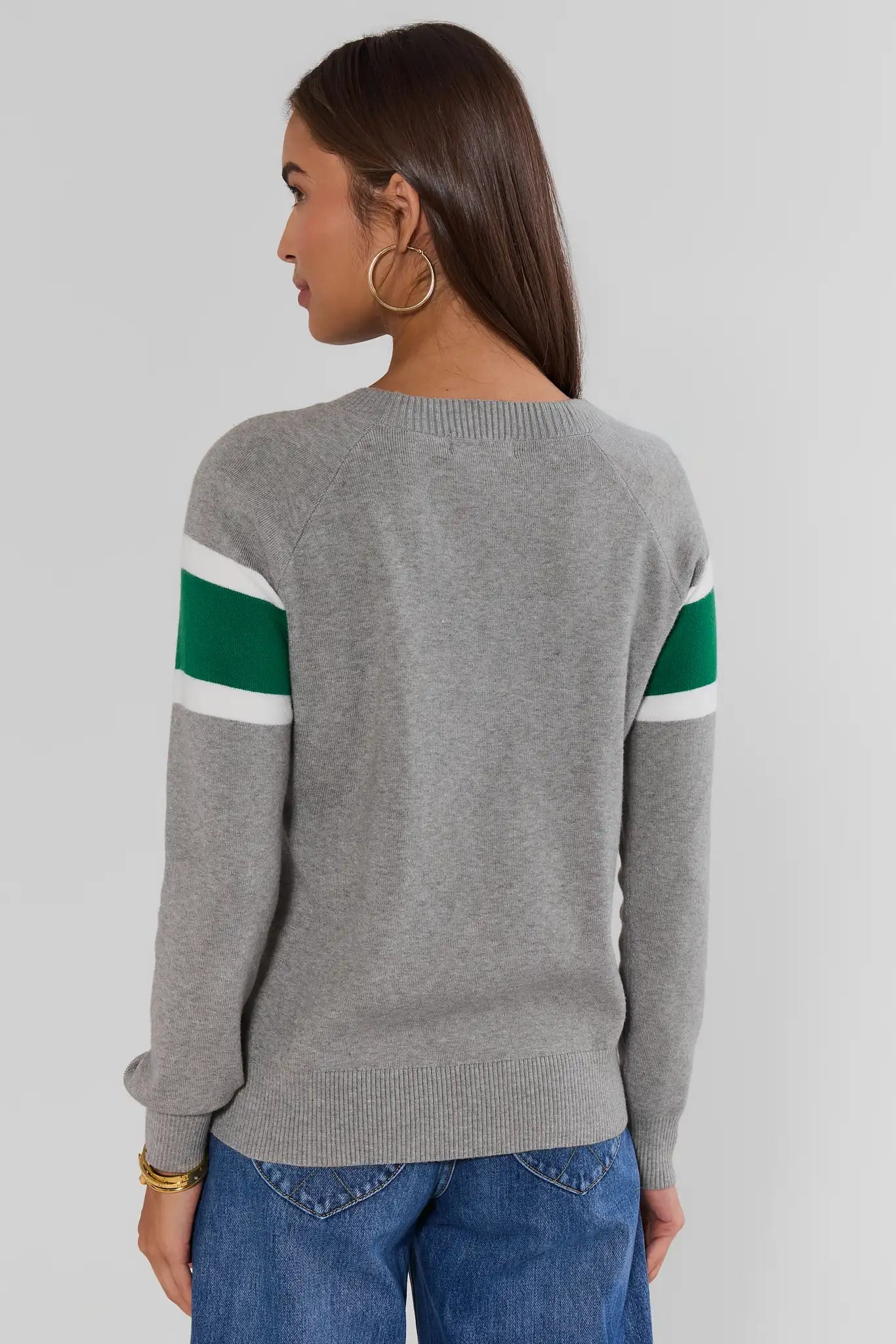 A woman shown from the back wearing a heather gray knit sweater with green and white stripes on the upper sleeves, paired with blue jeans, against a light gray studio background.