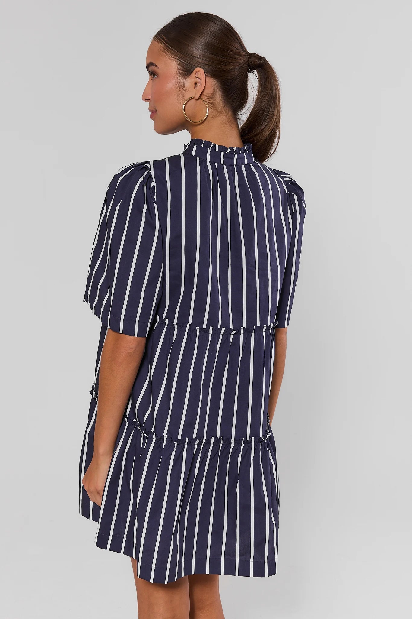 Woman standing wearing a navy and white striped dress against a plain background